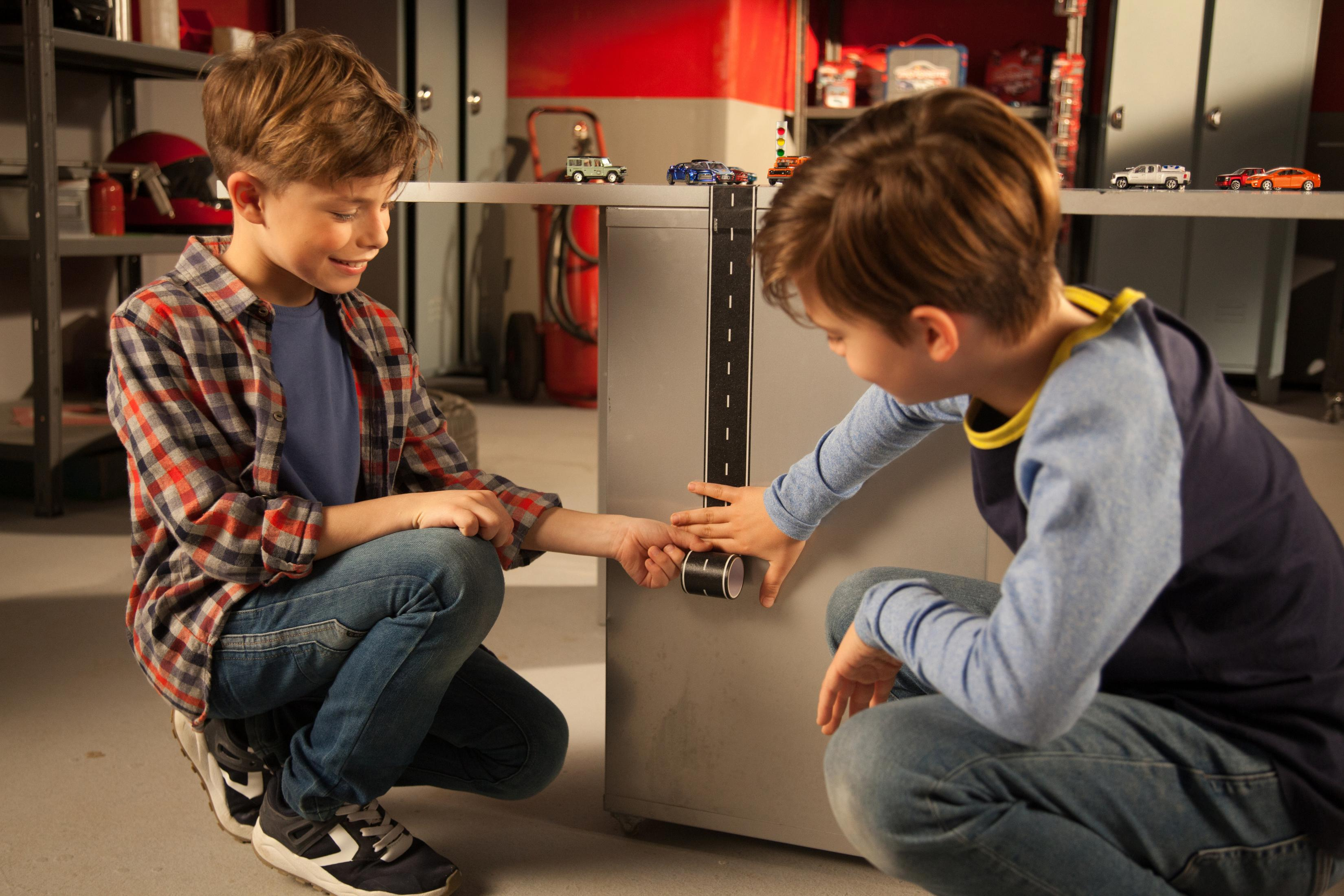 Dwóch chłopców bawi się samochodzikami i drogą na powierzchni.