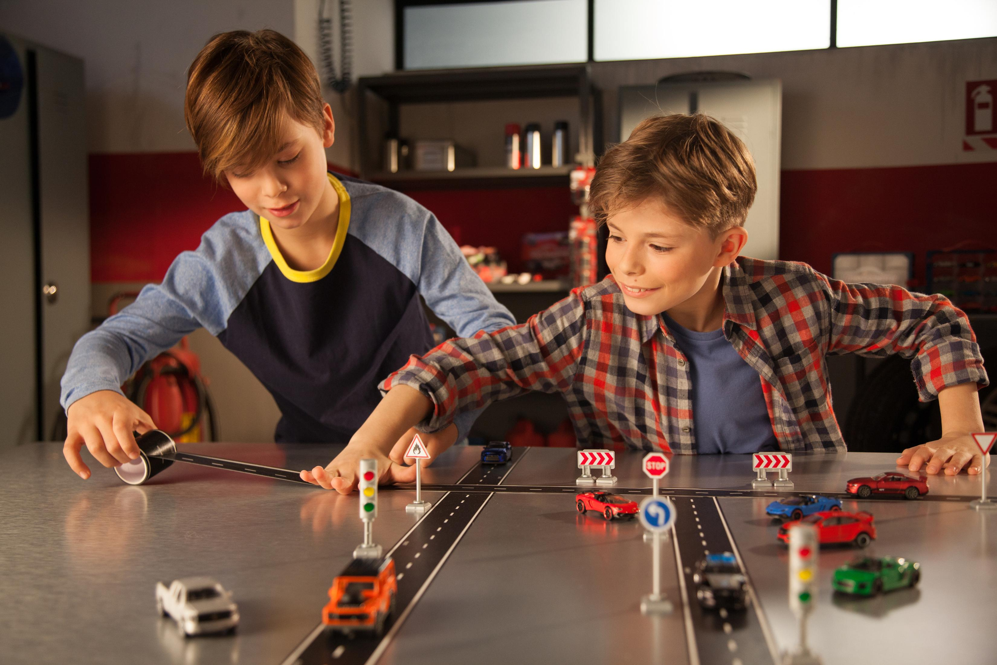 Dwóch chłopców bawiących się samochodzikami na modelu drogi ze znakami drogowymi.