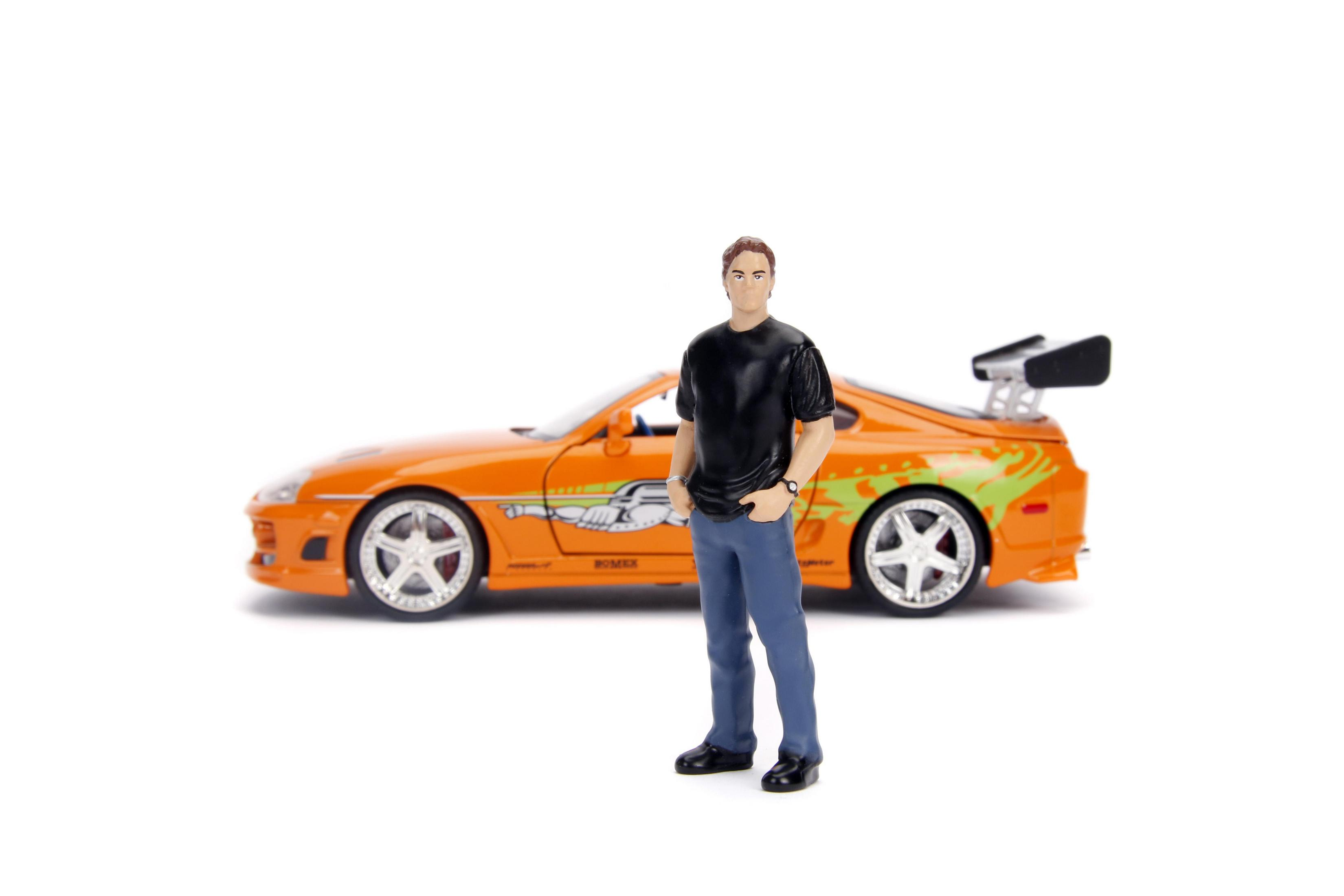 Eine Spielfigur eines Mannes, der vor einem orangefarbenen Sportwagen steht. Der Mann trägt ein schwarzes Hemd und Jeans.