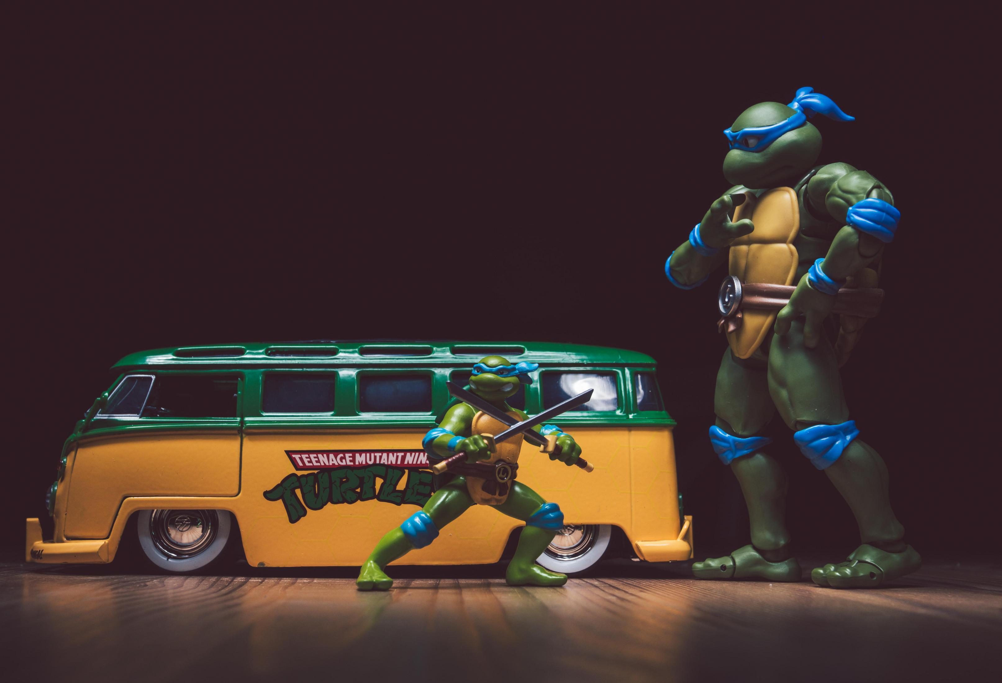 Zwei Teenage Mutant Ninja Turtles Actionfiguren und ein Van auf Holzoberfläche.