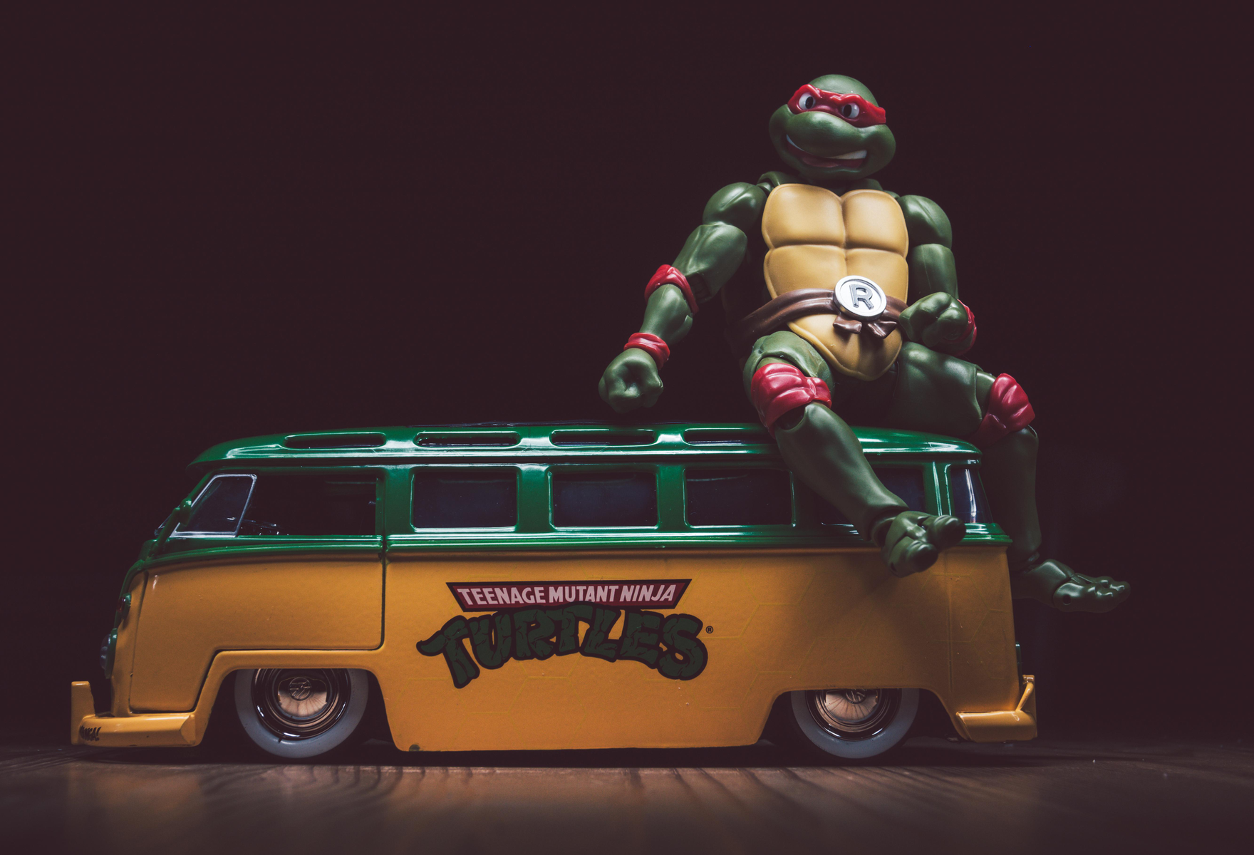 Eine Teenage Mutant Ninja Turtle-Figur sitzt auf einem gelb-grünen Van auf einer dunklen Holzoberfläche.