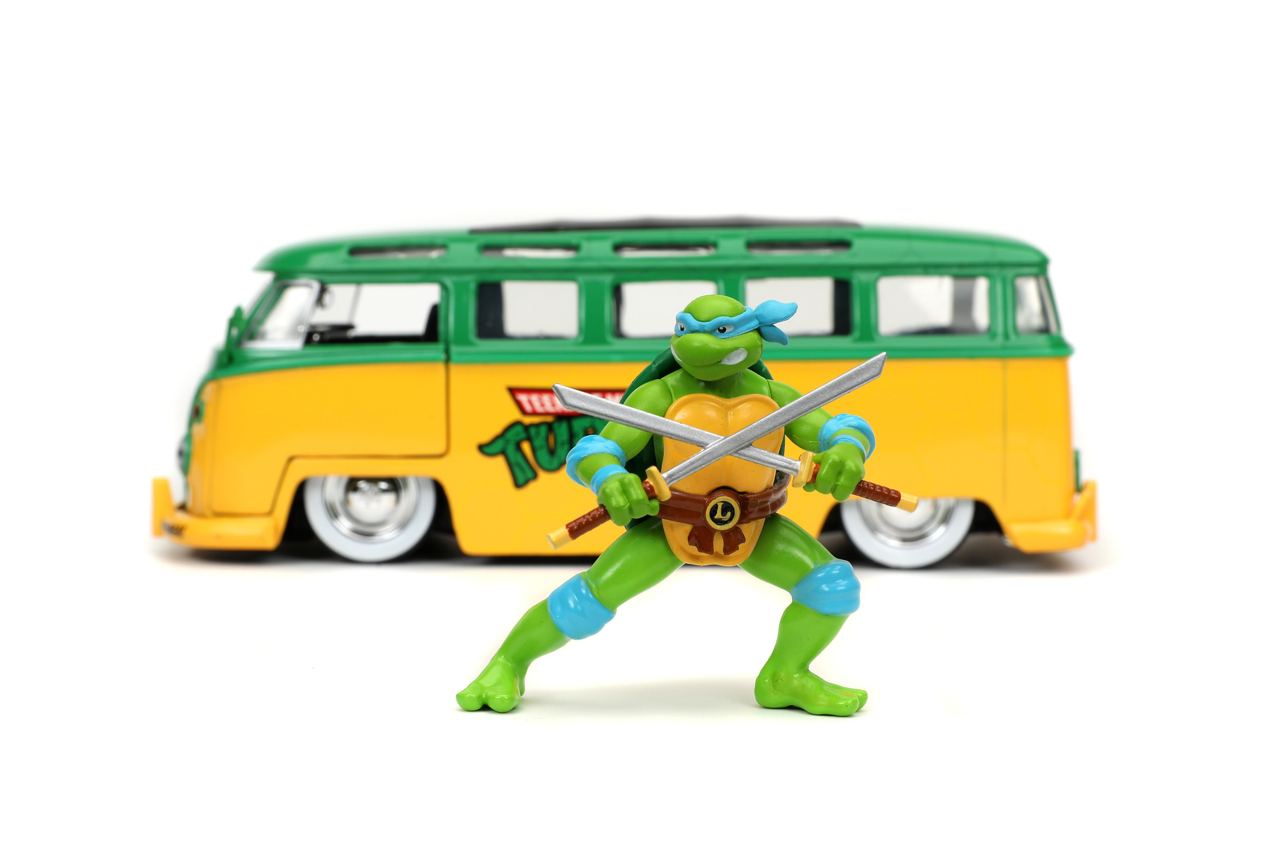 Teenage Mutant Ninja Turtle Spielzeug, Schwerter haltend, vor einem grünen und gelben Van.