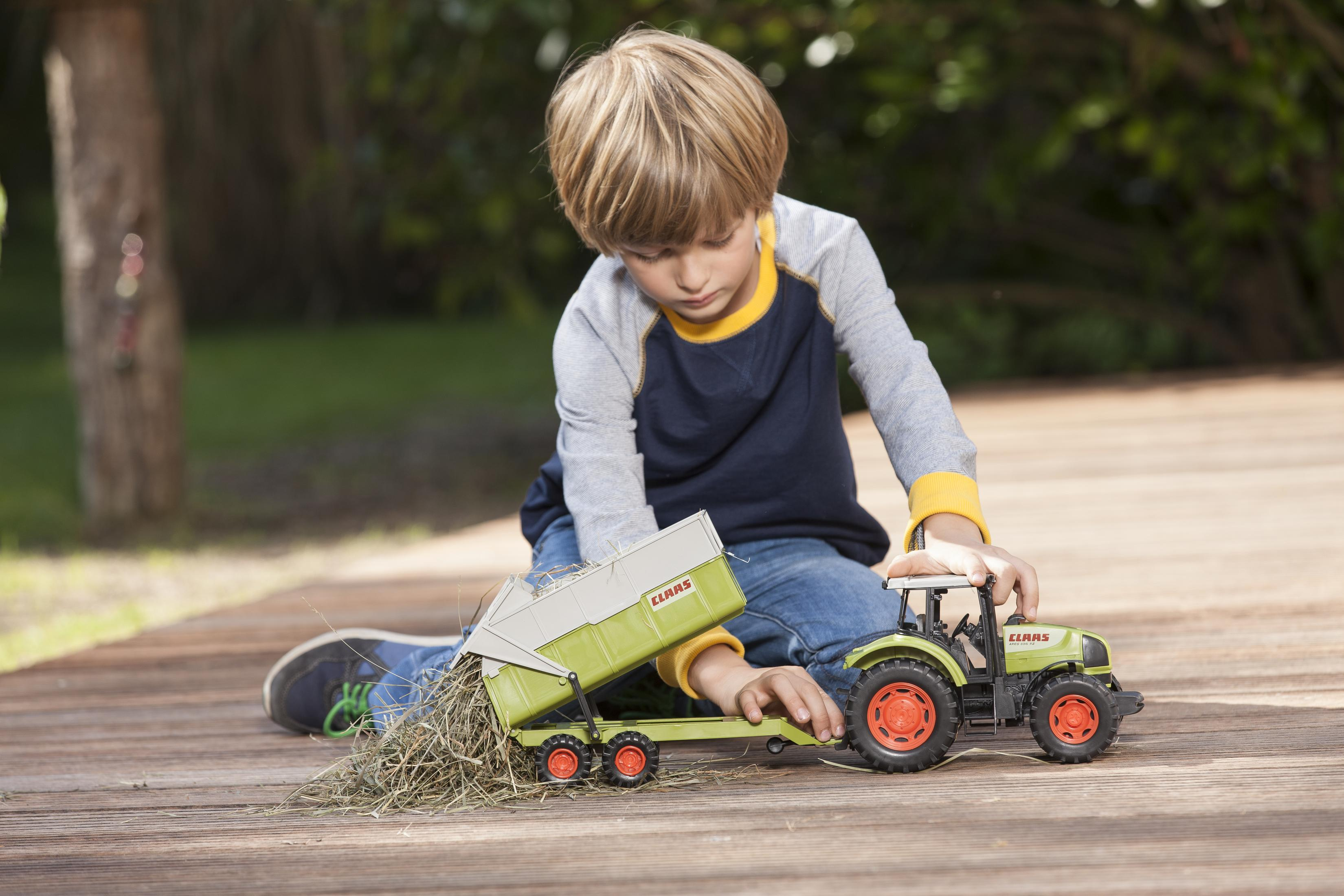 Chłopiec bawiący się zabawką ciągnikiem i przyczepą na drewnianym tarasie.