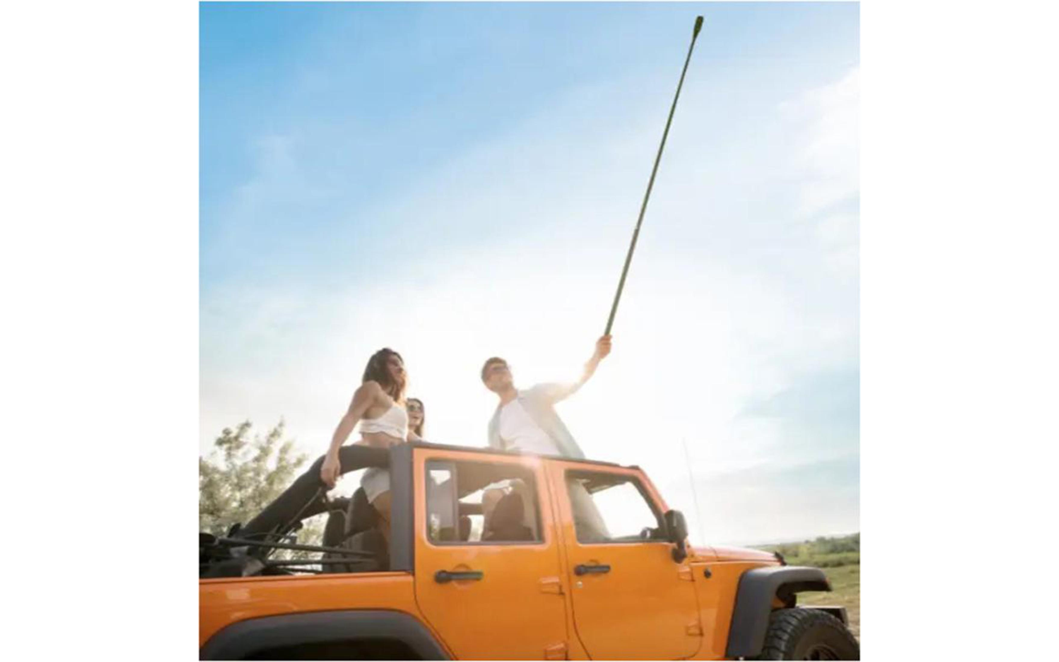 Persone su una Jeep arancione tengono in alto un lungo palo. Giornata di sole. Cielo sereno.