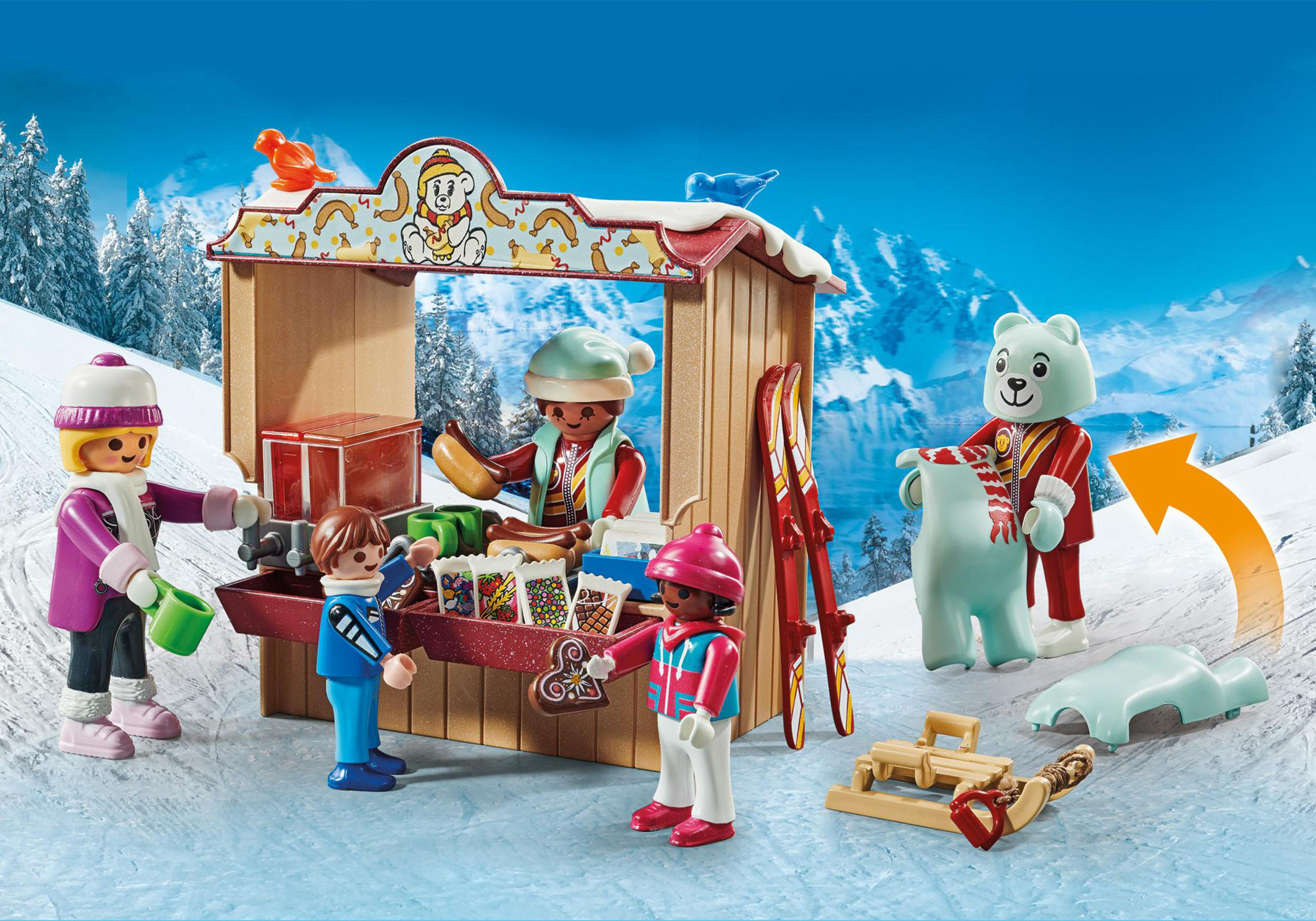 Scena invernale Playmobil con personaggi, un orso, un negozio e uno sfondo montuoso innevato.