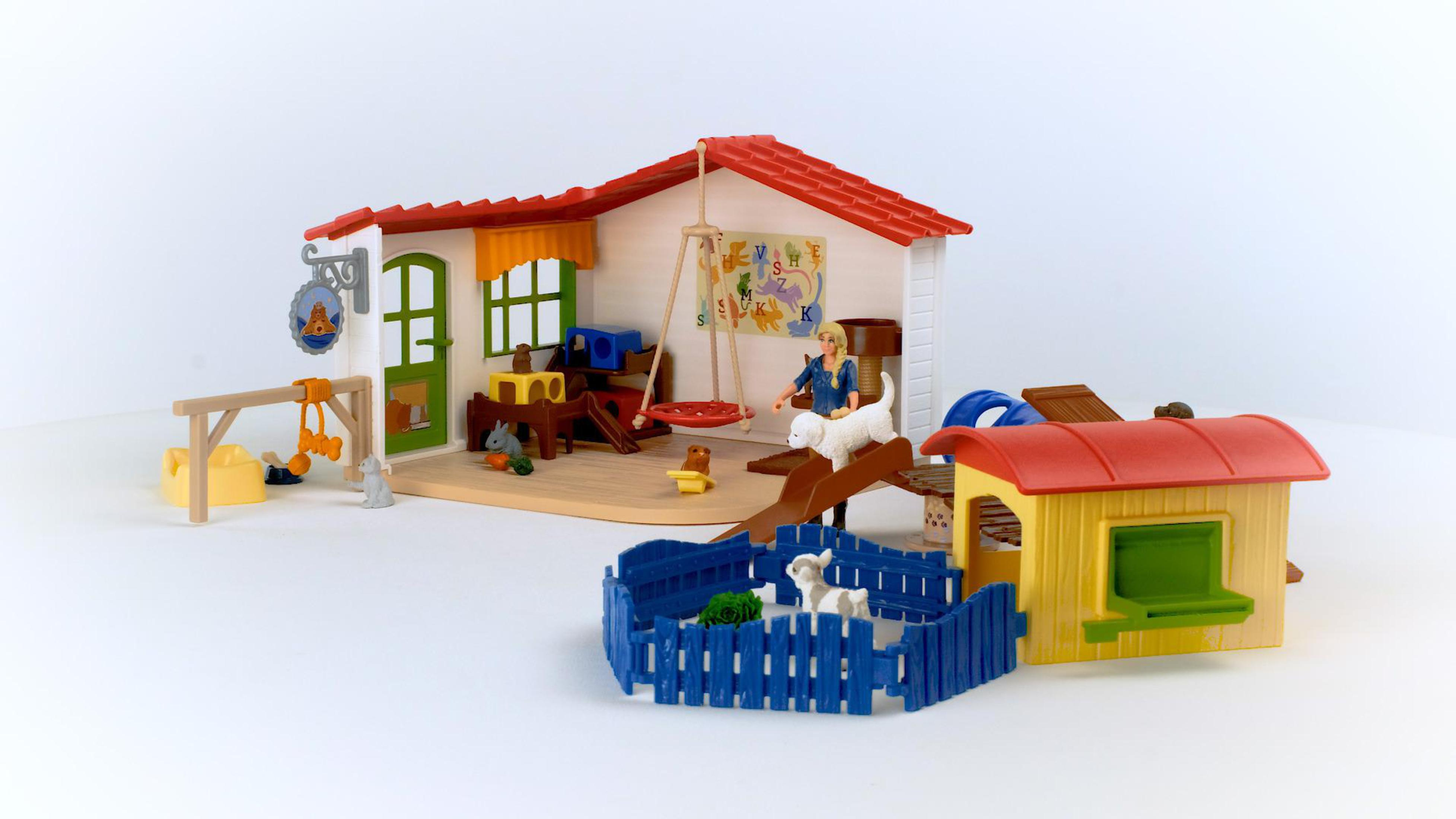 Scena Playmobil: Un asilo per cani con giocattoli, persone e cani dentro e intorno a un edificio.