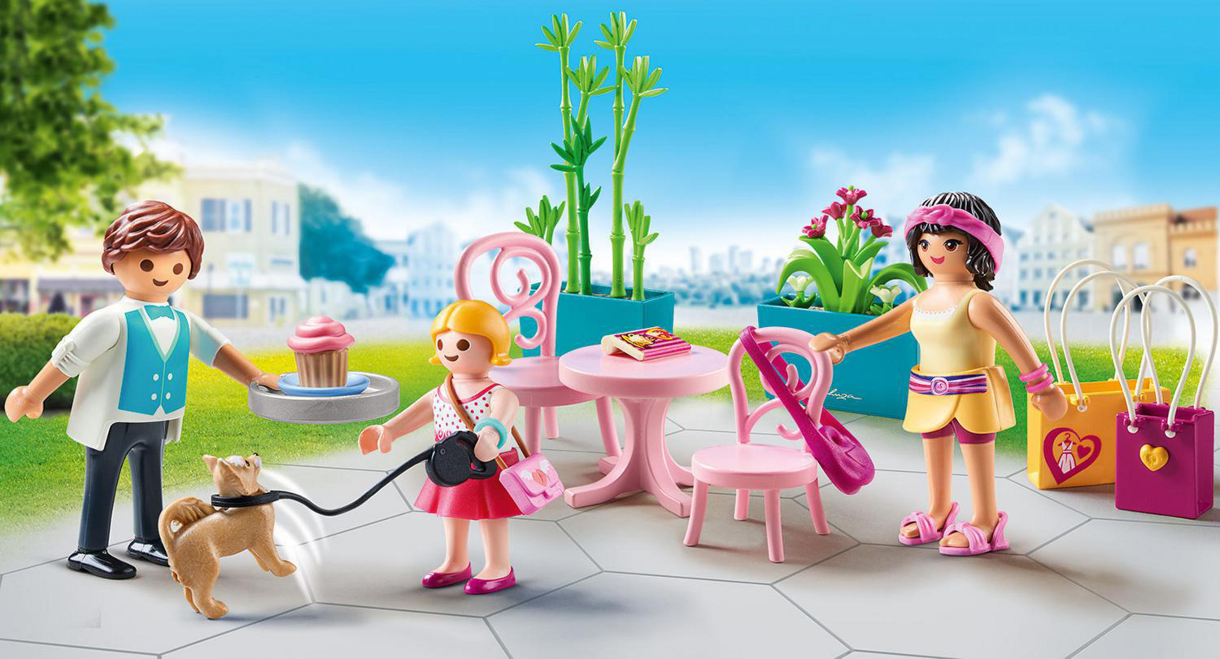 Playmobil-Figuren: Familie in einem Café. Die Szene umfasst einen Hund, Cupcakes und Einkaufstaschen.