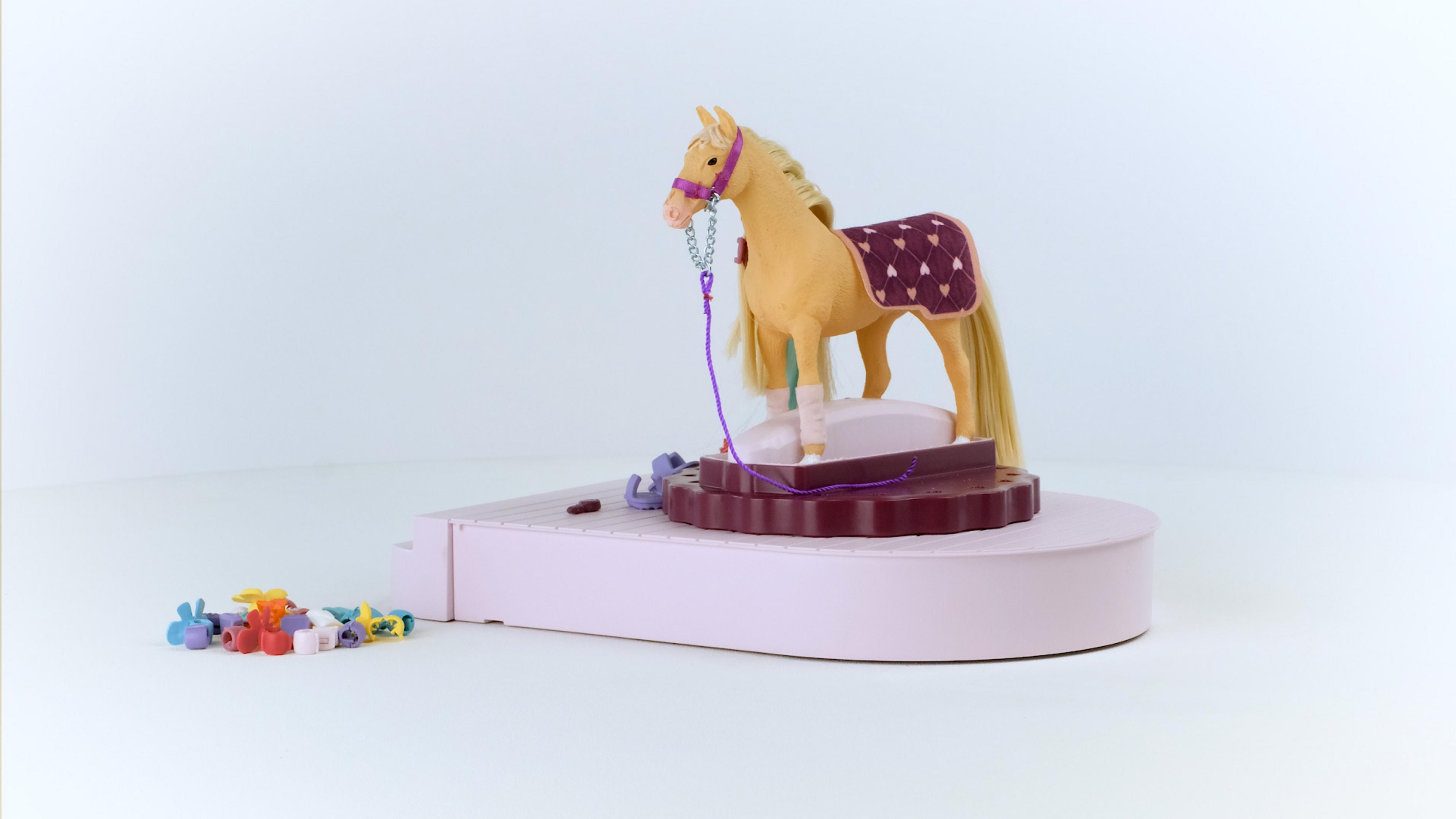 Toy horse on a stage. The horse is tan with a purple blanket. White background.