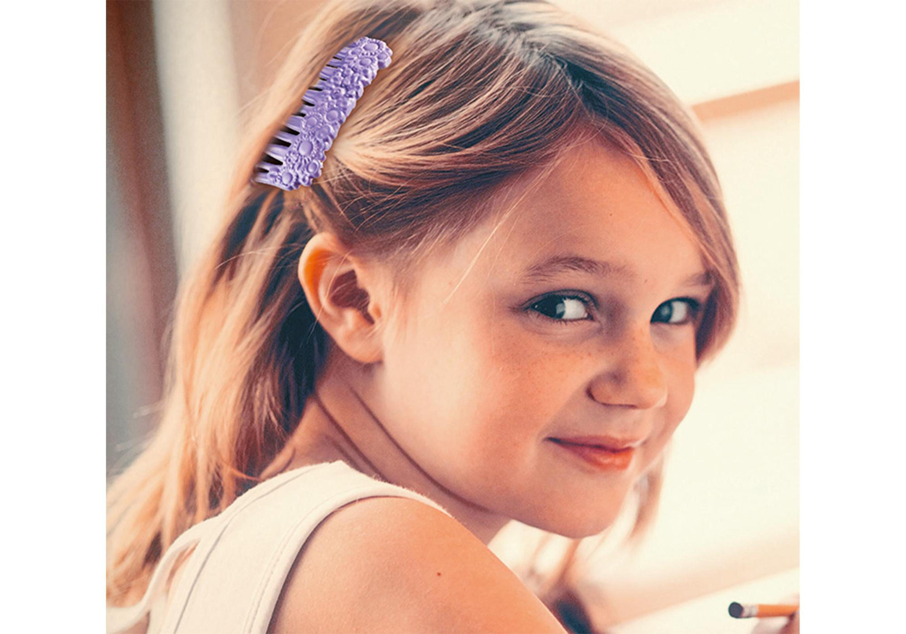 Una bambina con i capelli biondi, che tiene un pettine viola tra i capelli, sorride alla fotocamera.