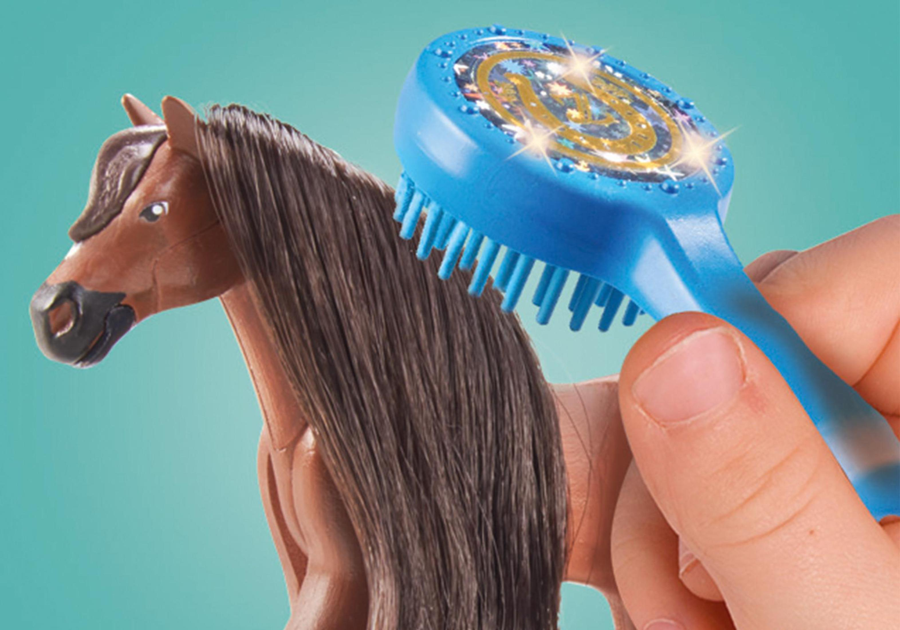 Una mano che tiene una spazzola blu che cura un cavallo marrone.
