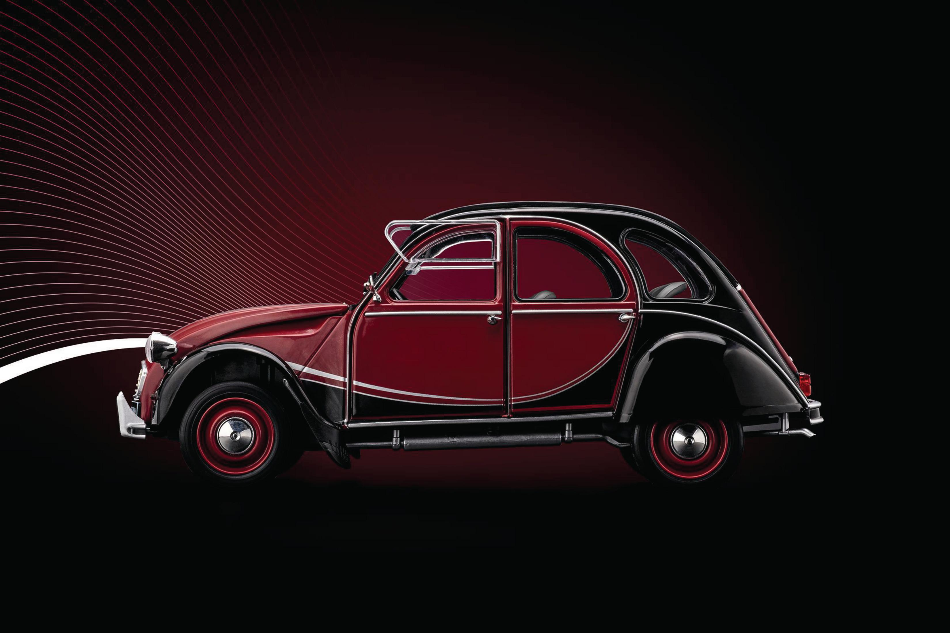 Ein rot-schwarzes Spielzeugauto, ein Citroen 2CV, mit schwarzem und rotem Hintergrund.
