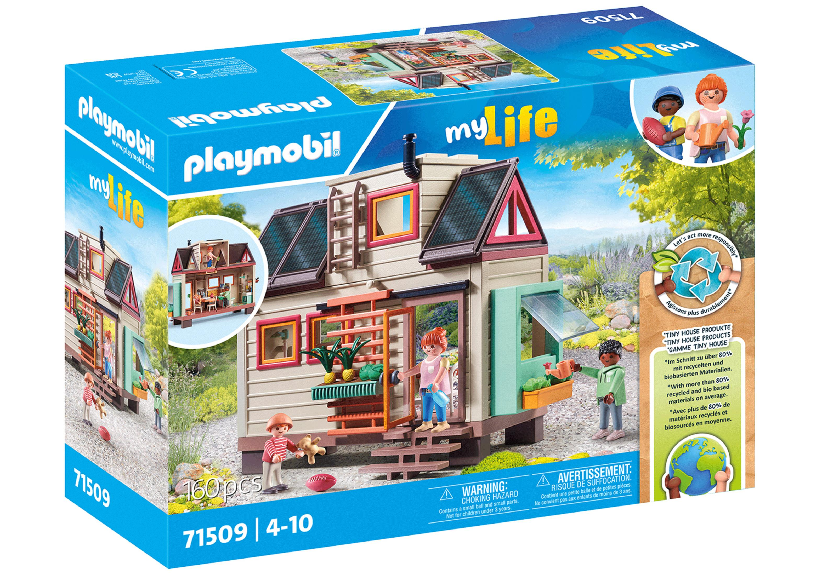 Playmobil-Box: kleines Haus mit Figuren. Grüne Pflanzen, Gebäude mit rotem Dach, sonnige Umgebung.