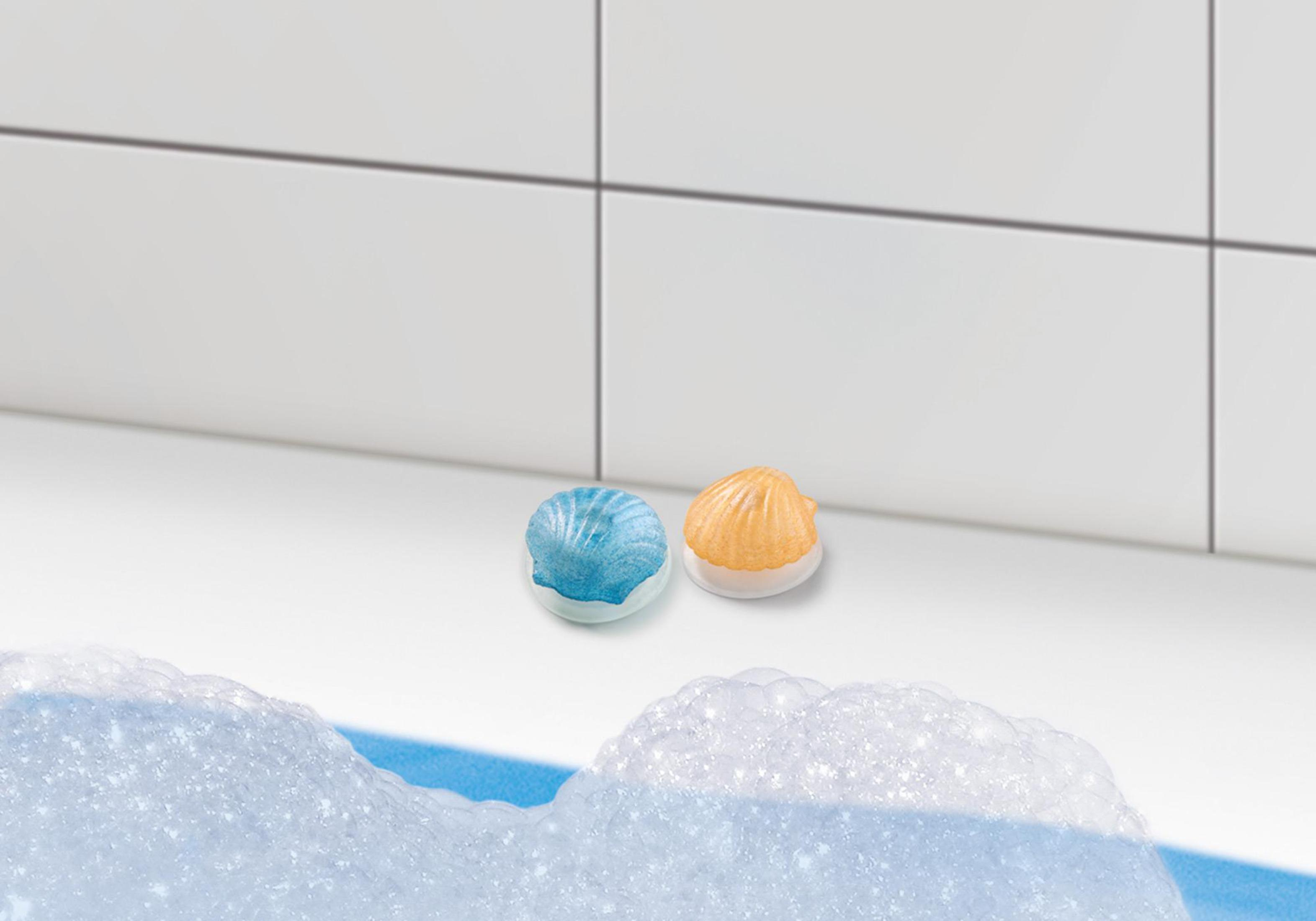 Zwei muschelförmige Badekugeln auf weißer Oberfläche, mit Blasen im Vordergrund.