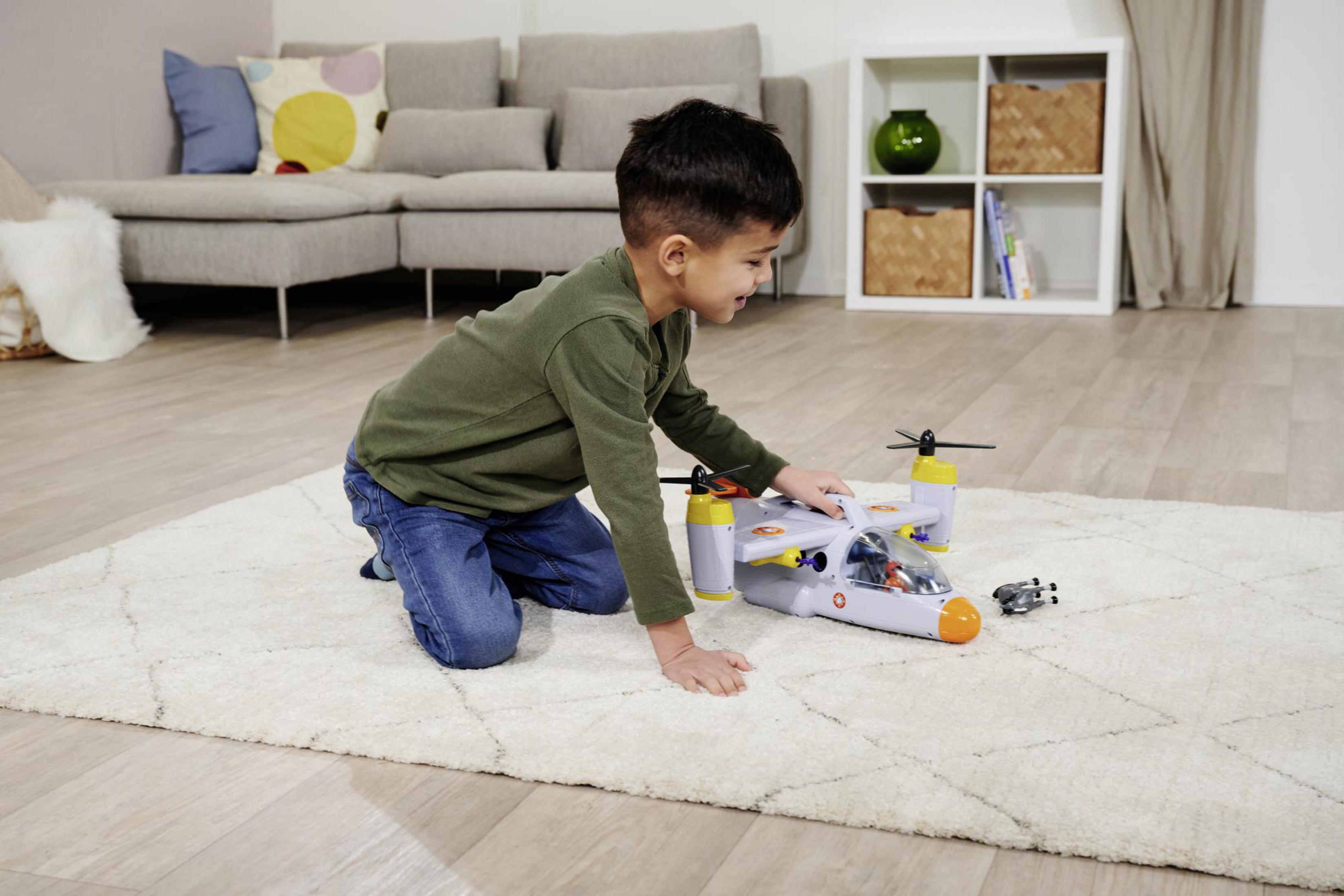 Ein kleiner Junge spielt mit einem Spielzeug-Hubschrauber und einem kleinen Auto auf einem Teppich.