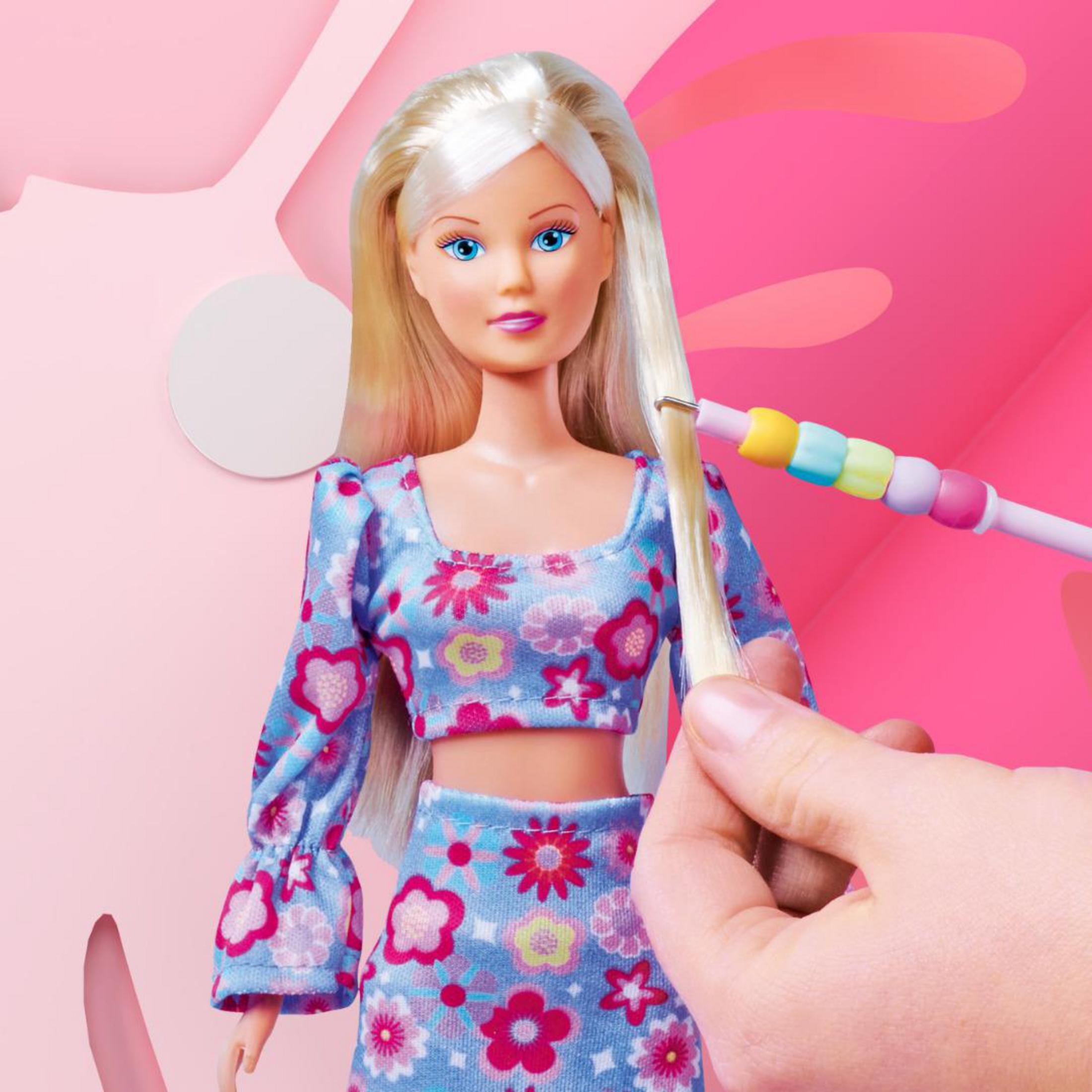 Eine Puppe mit blonden Haaren, blauen Augen und einem Blumenkleid wird mit einem Haaraccessoire gestylt.