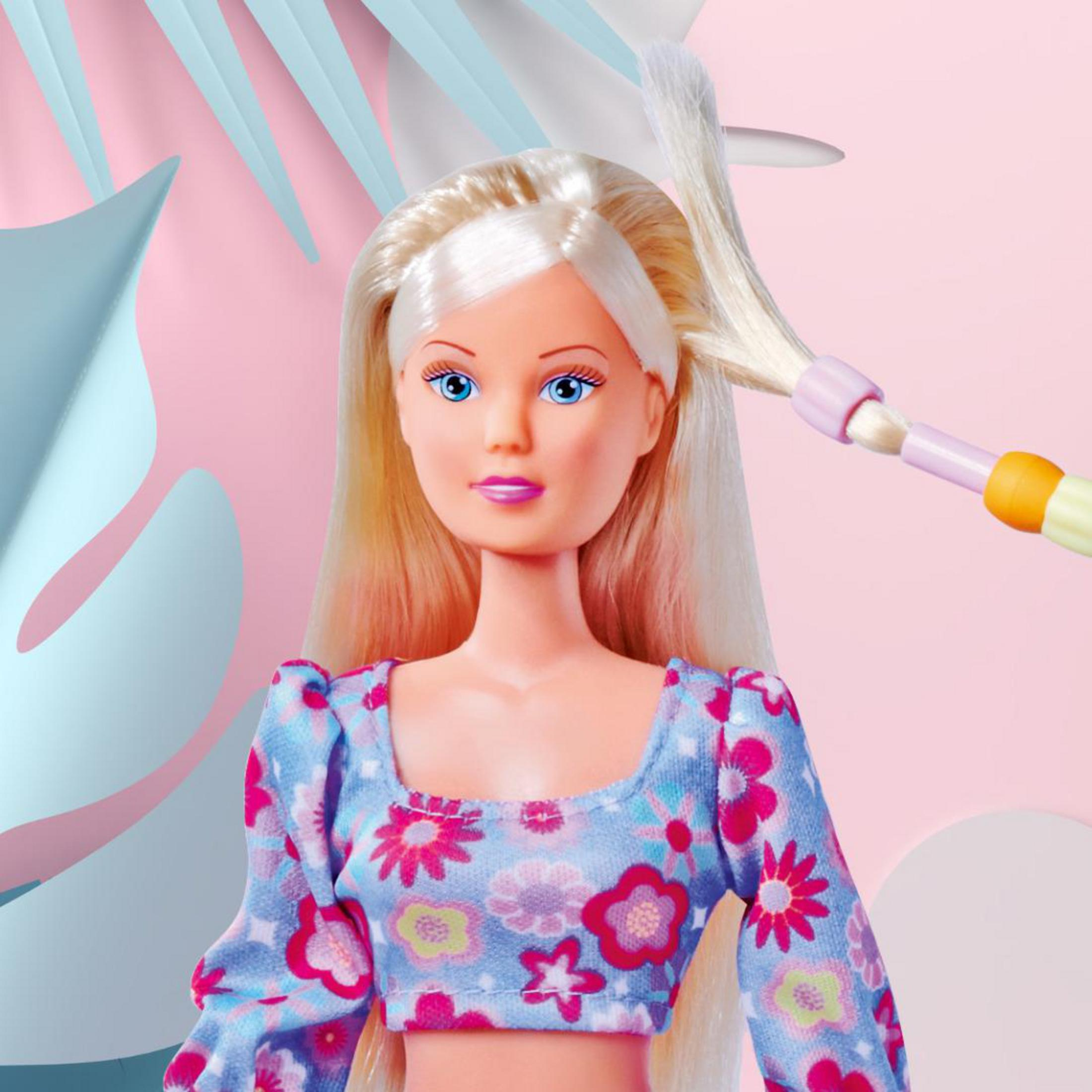 Eine Puppe mit blonden Haaren wird gestylt. Sie hat blaue Augen und ein geblümtes Oberteil. Rosa und blauer Hintergrund.