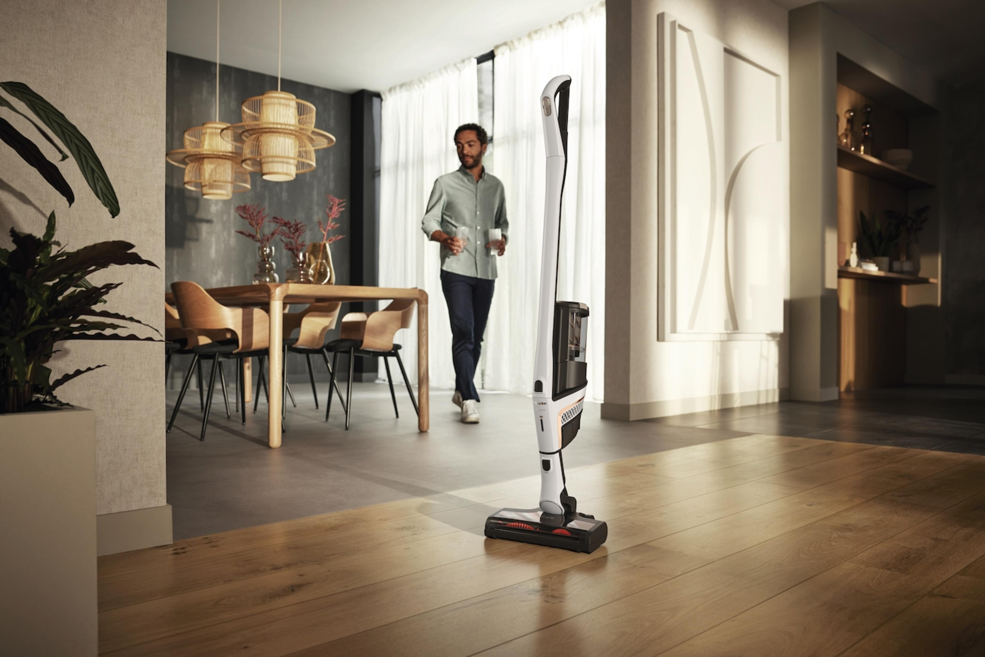Mann benutzt einen weißen kabellosen Staubsauger in einem modernen Wohnzimmer.