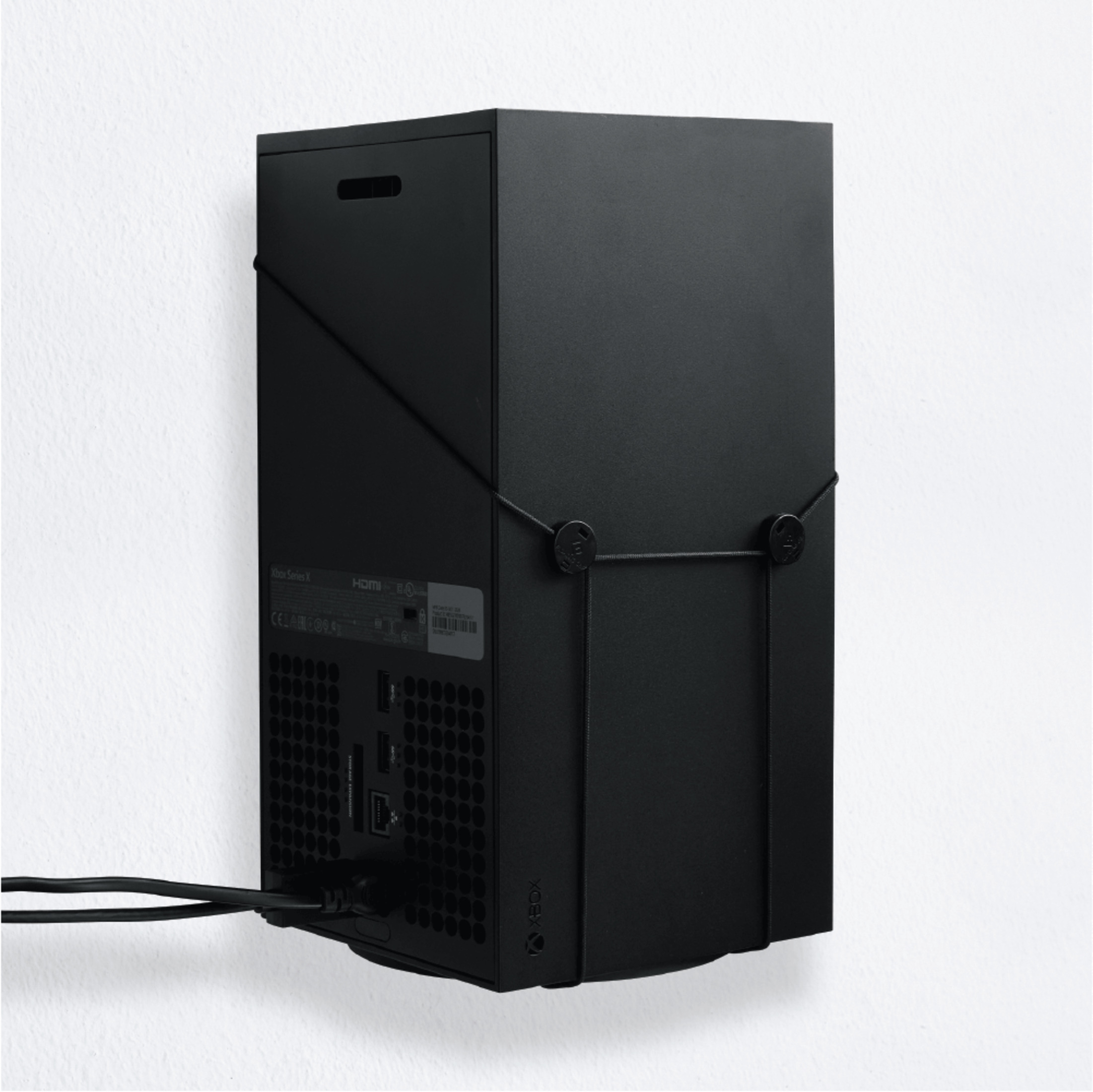 Czarna konsola Xbox Series X zamontowana na ścianie, z kablami. Widoczny tylny panel.
