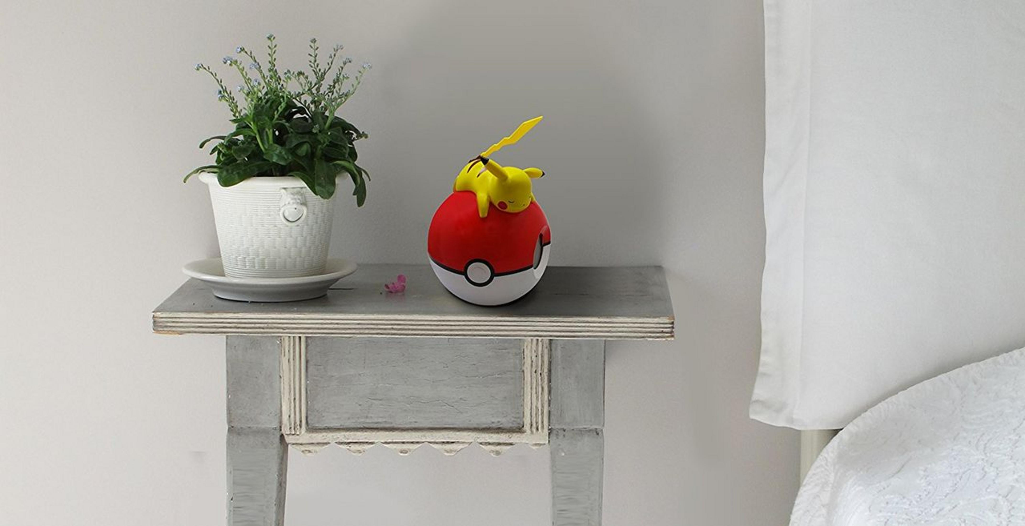 Pikachu na Pokéballu na szarym stole z rośliną i białą ścianą.