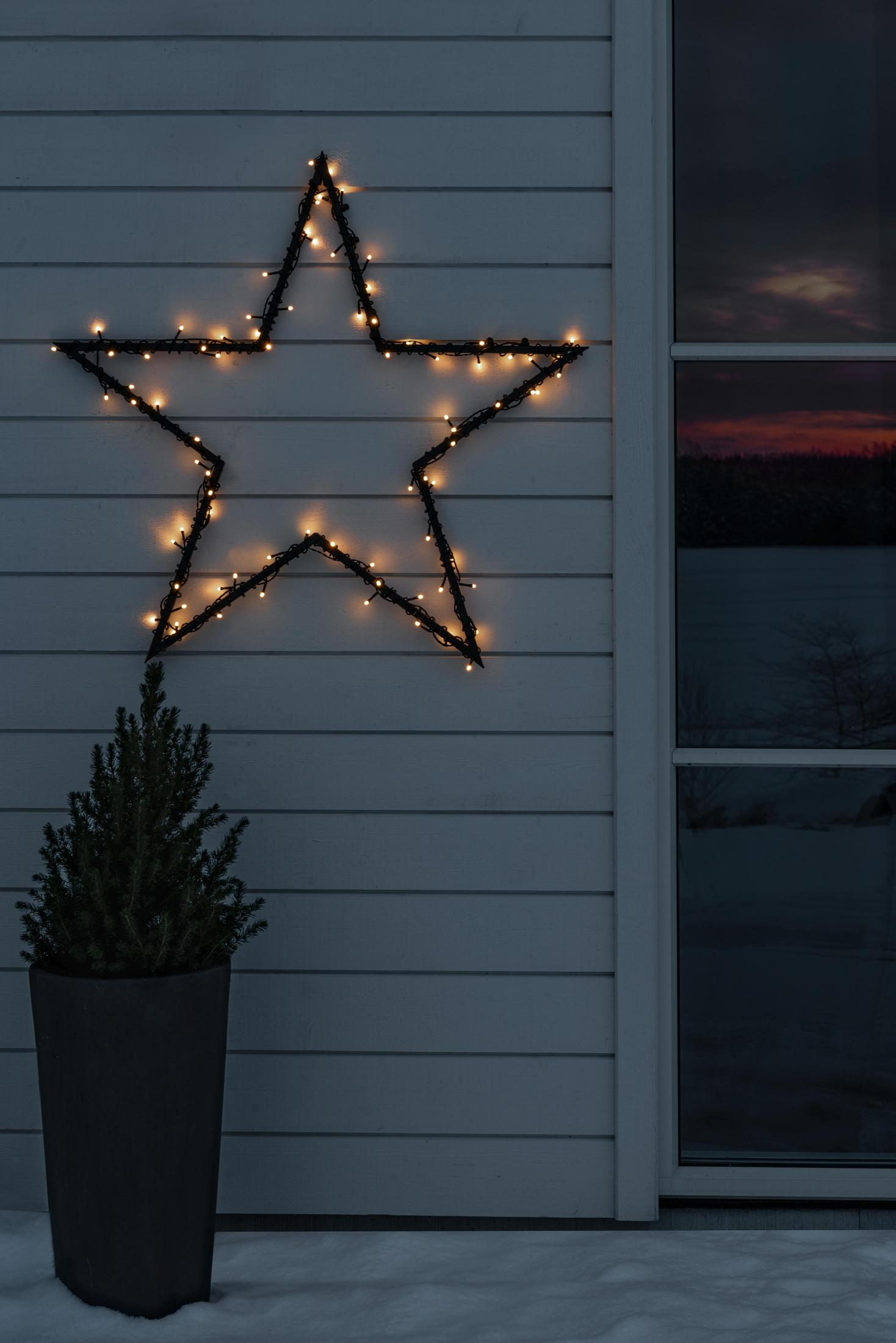 Sternförmige Weihnachtsbeleuchtung an einer Wand mit kleinem Baum darunter.