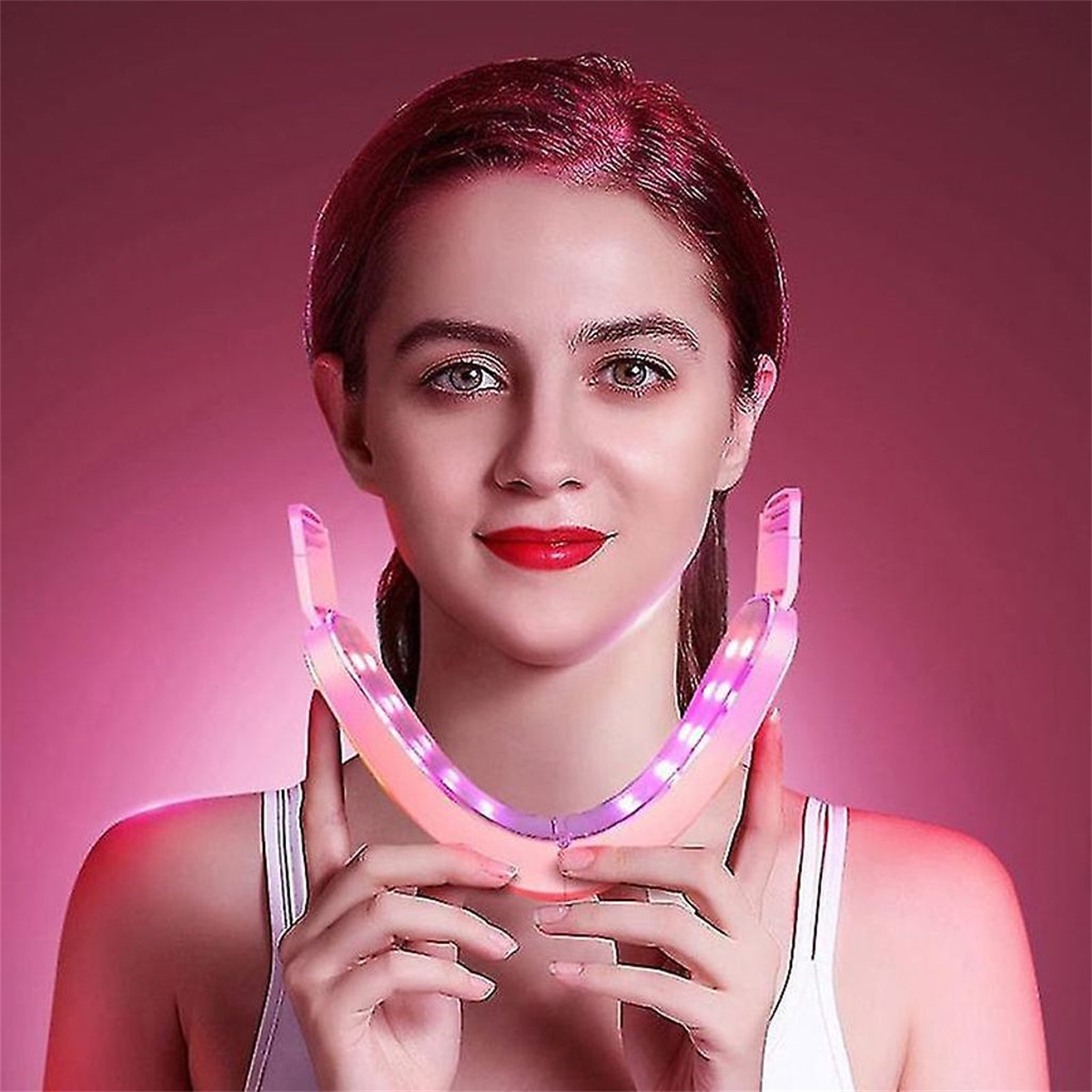 Eine Frau mit rotem Lippenstift trägt ein rosa LED-Gesichtsgerät.