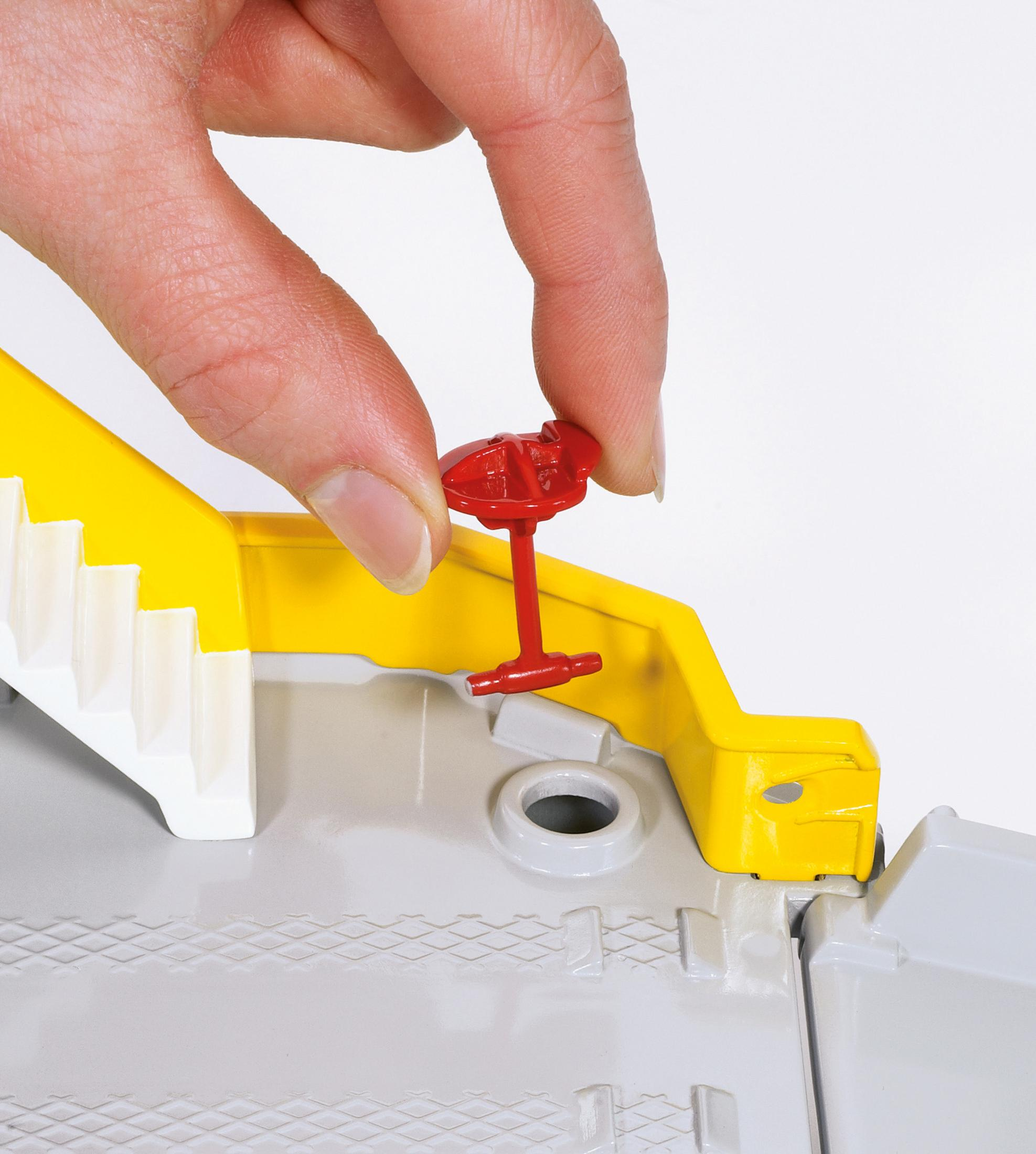 Ręka umieszcza czerwony element w zabawce konstrukcyjnej. Żółte i szare konstrukcje.