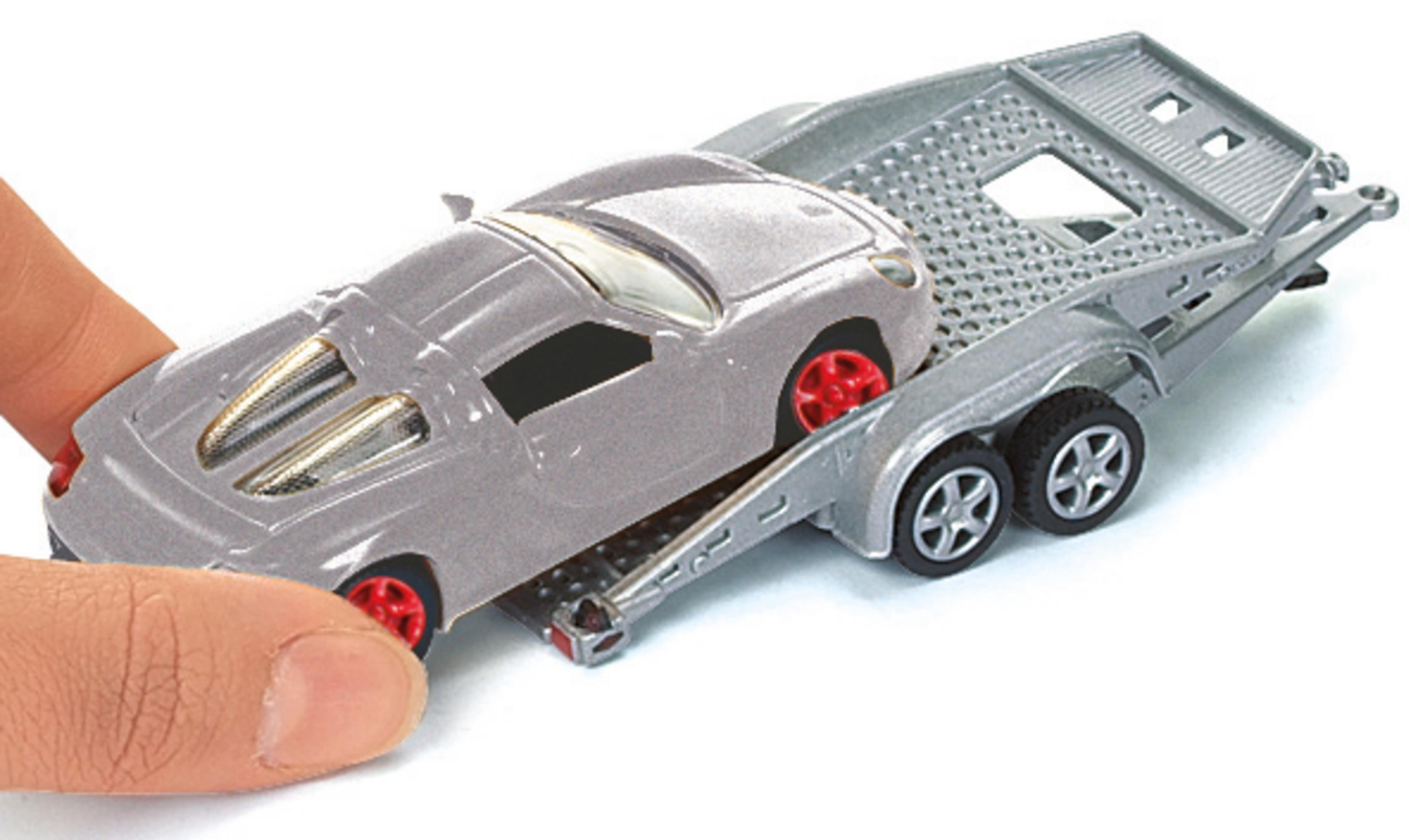 Zabawkowy samochód ładowany na srebrną lawetę. Samochód jest szary z czerwonymi kołami.