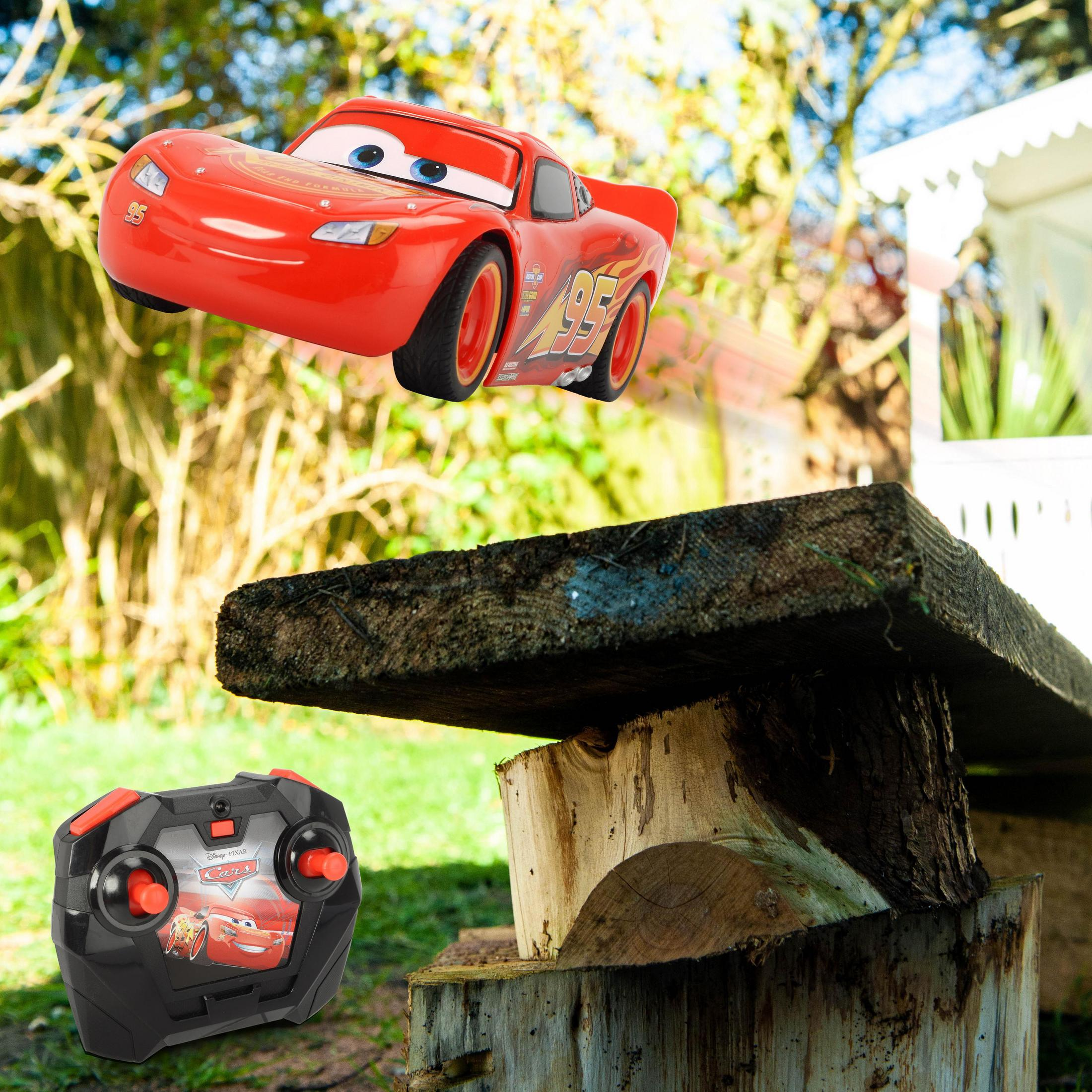 Un coche de juguete rojo salta sobre estructura de madera. Mando a distancia en primer plano.