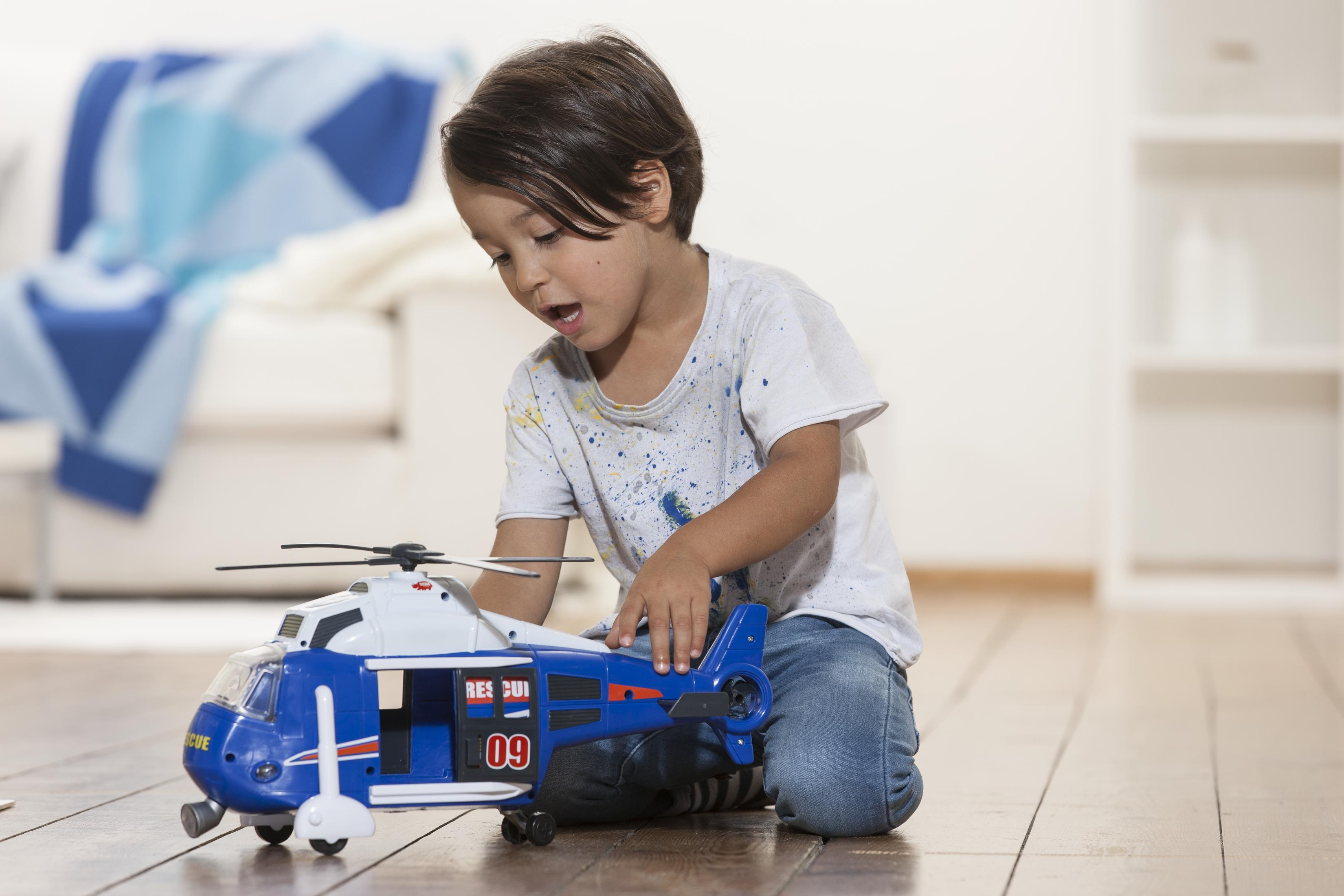 Ein kleiner Junge spielt auf einem Holzboden mit einem blau-weißen Spielzeug-Hubschrauber.