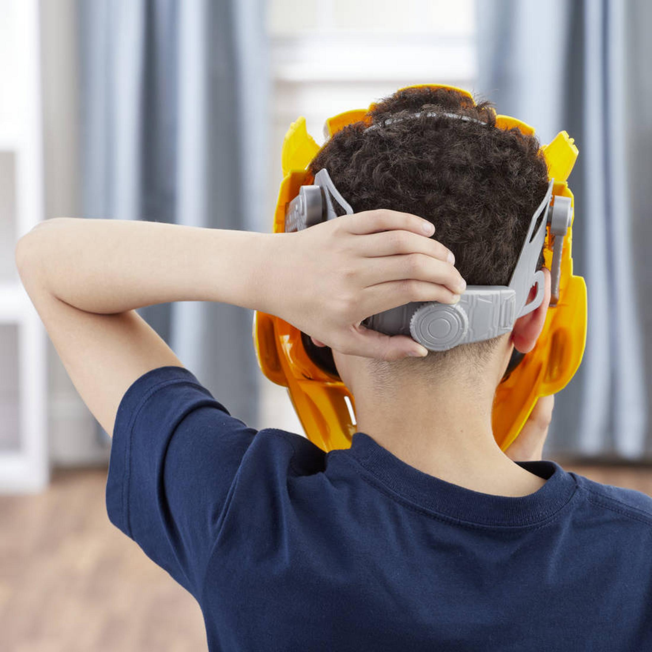 Ein Kind trägt eine gelbe Maske, von hinten gesehen. Die Maske bedeckt Kopf und Gesicht.
