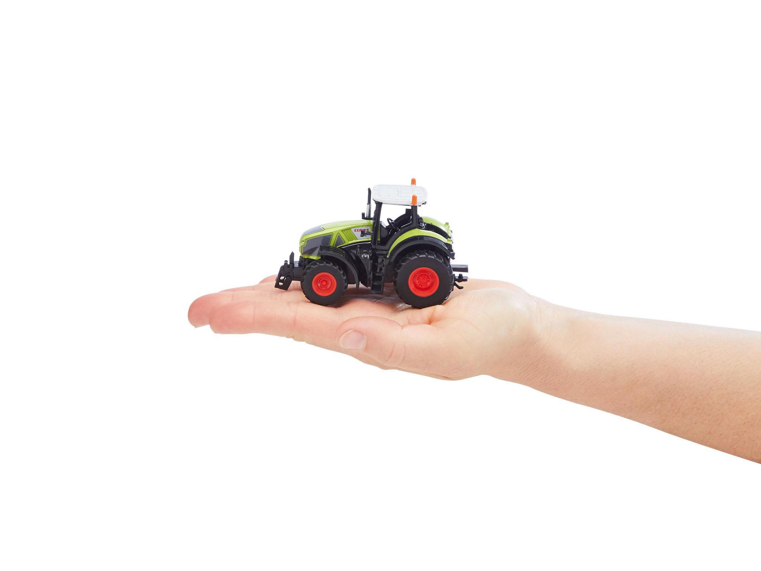 Tractor de juguete verde y negro en la mano, fondo blanco. Ruedas y detalles rojos.