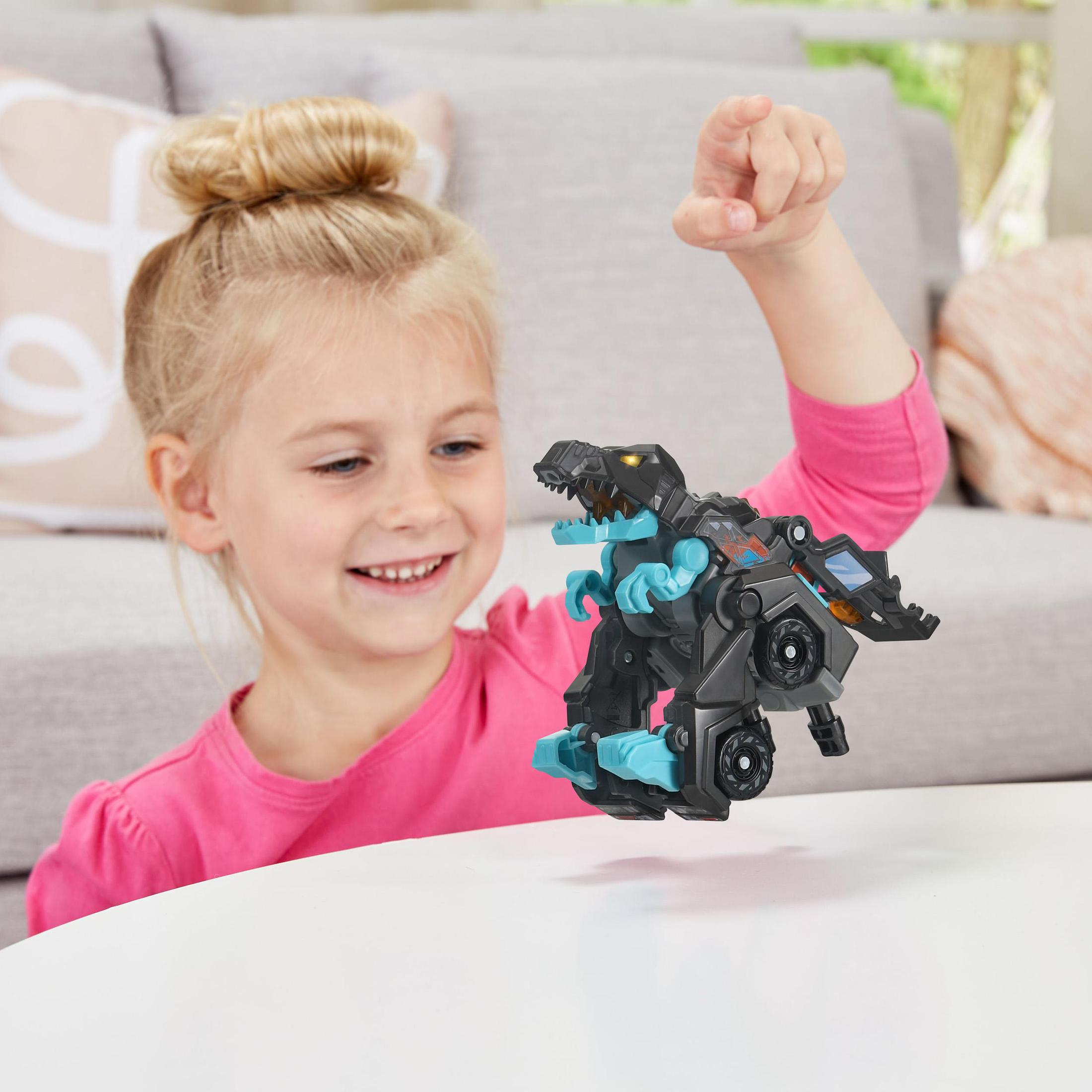 Ein lächelndes Mädchen spielt mit einem schwarzen und blauen Spielzeug-Dinosaurier. Weißer Tisch.