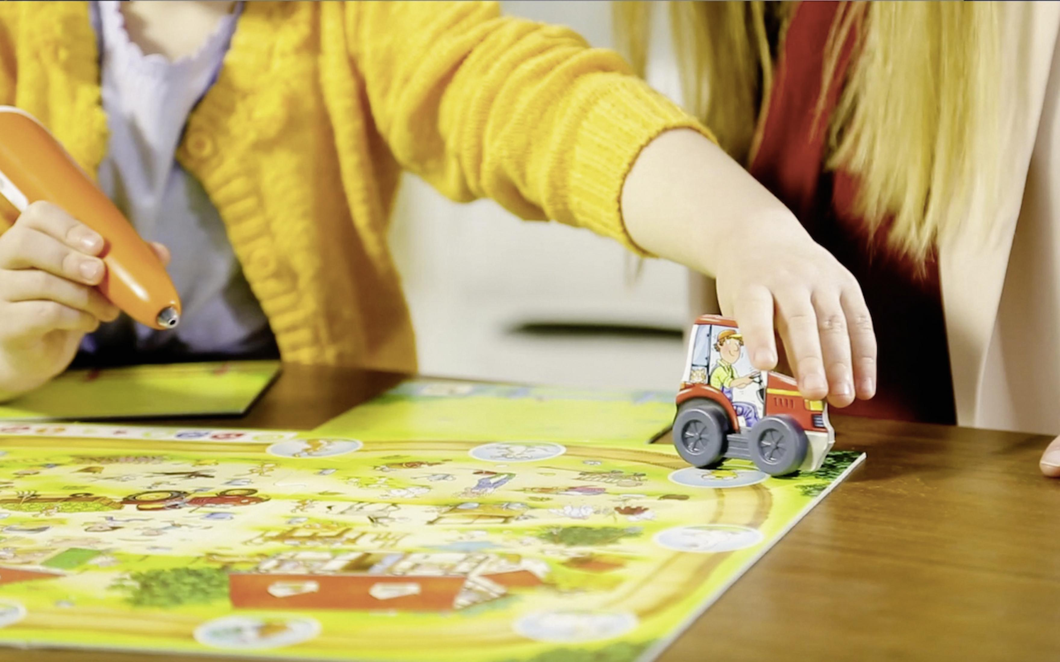 Kinder spielen mit einer Spielzeug-Bauernhofszene. Ein Kind hält einen Stift, das andere einen Traktor.