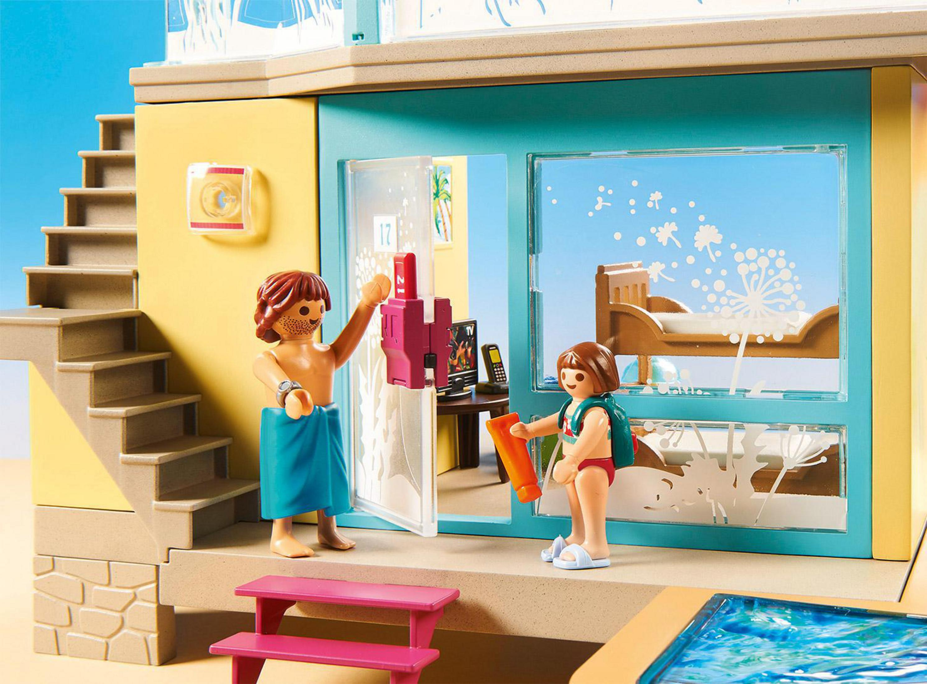 Escena de Playmobil: dos figuras, una en toalla y otra con mochila, cerca de una casa.
