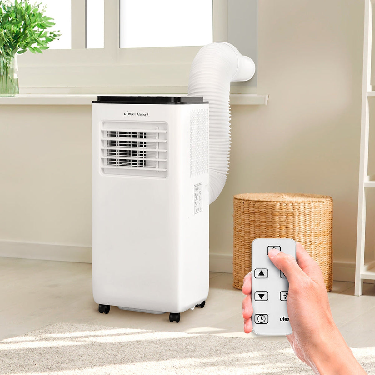 Biały przenośny klimatyzator z wężem wydechowym. Pilot w dłoni.