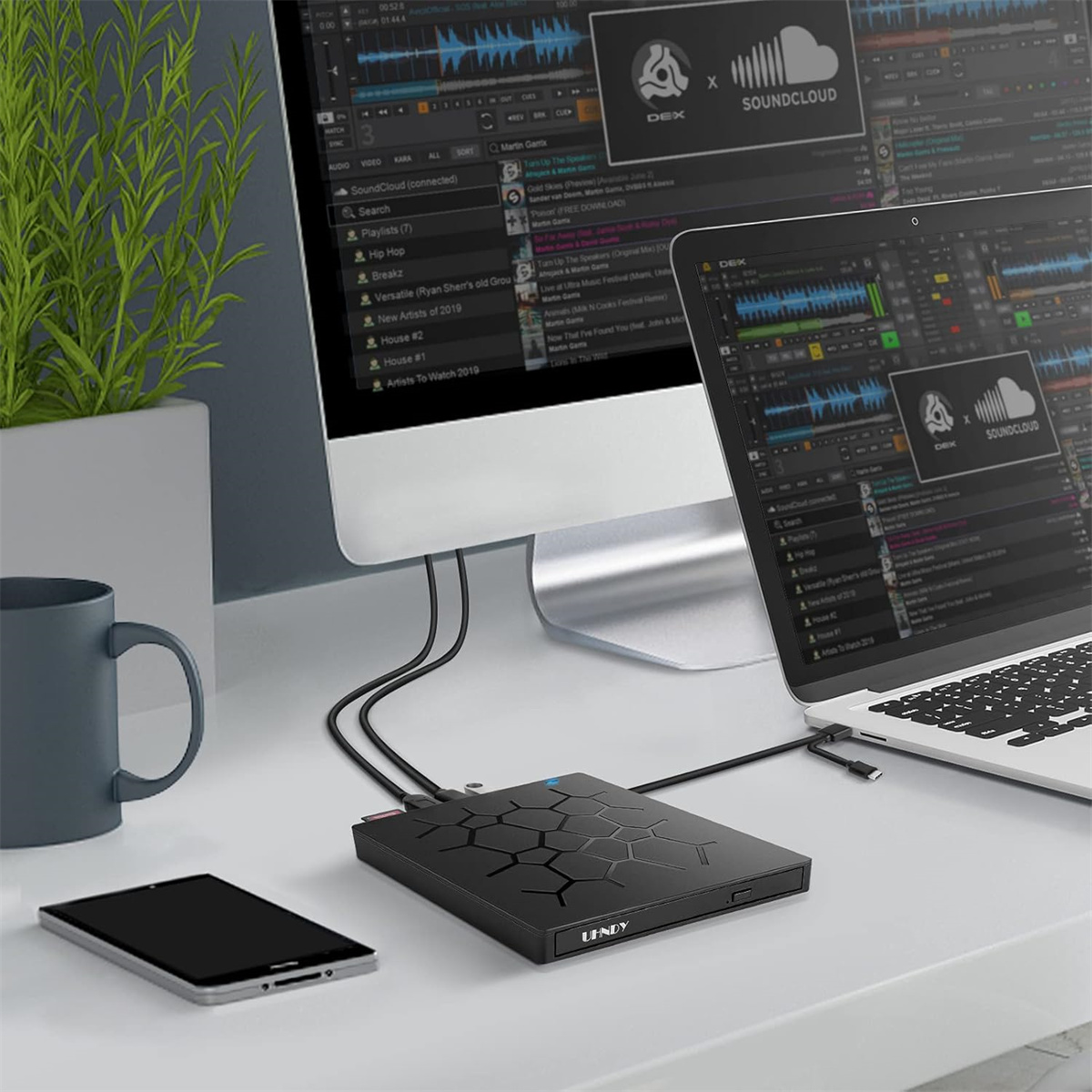 Ein Schreibtisch-Setup mit Laptop, Telefon, externem Laufwerk und Monitor. Kabel sind angeschlossen.