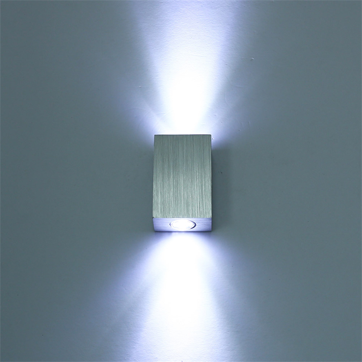Eine silberne, rechteckige Wandleuchte, die hellweißes Licht nach oben und unten ausstrahlt.