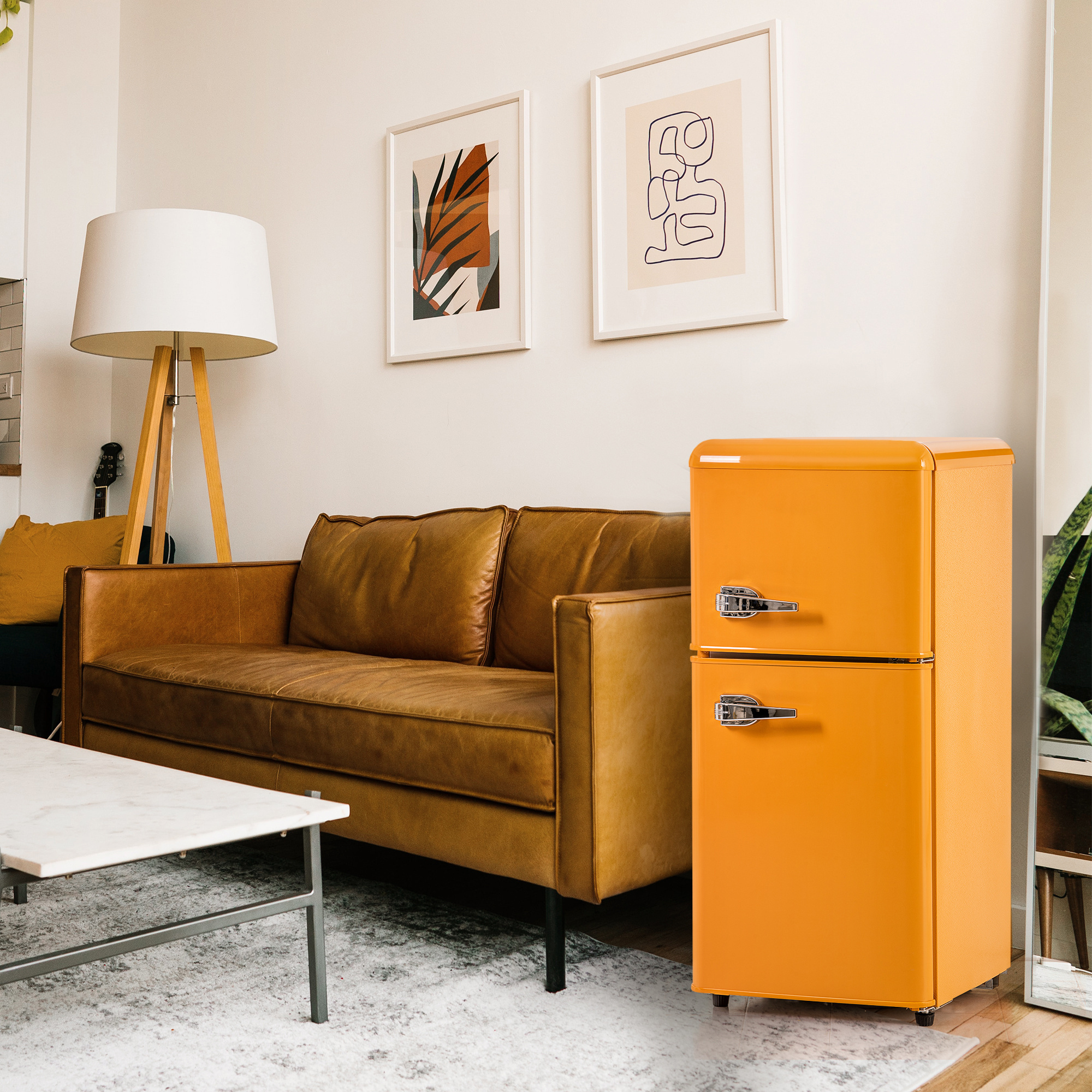Wohnzimmerszene mit braunem Sofa, orangefarbenem Kühlschrank, Kunstdrucken und einer hölzernen Stehlampe.