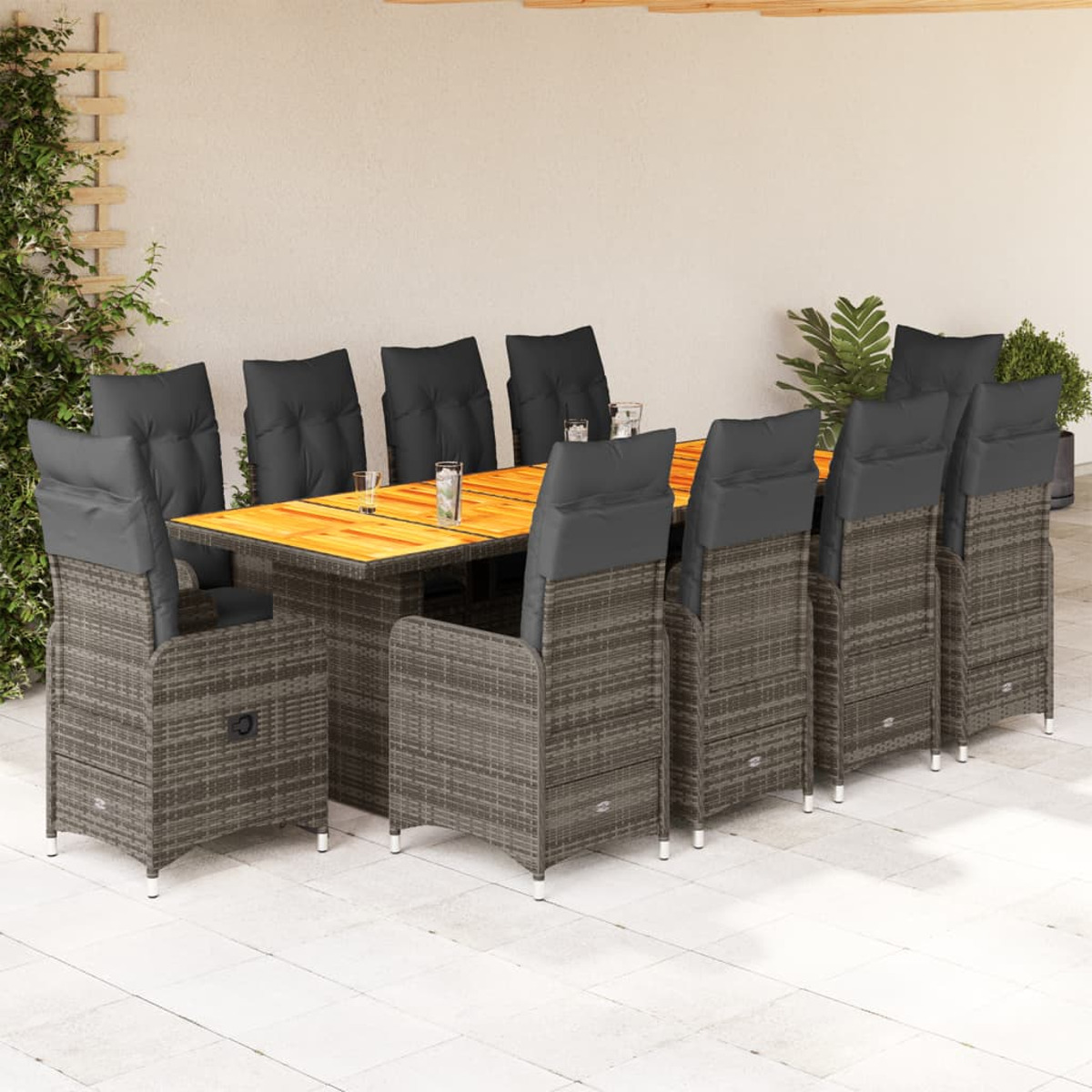 Un set da pranzo per patio con un tavolo di legno e sedie in vimini grigie con cuscini neri. Il pavimento è chiaro.