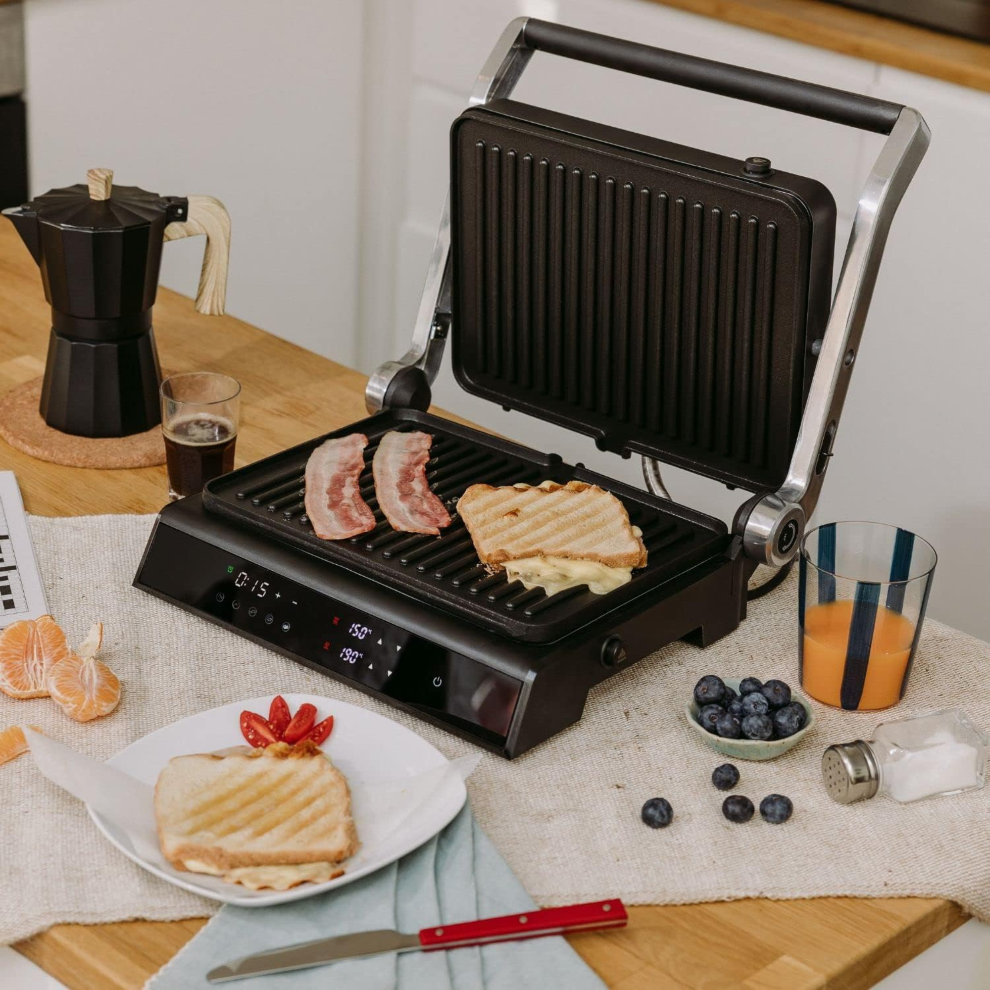Una griglia per sandwich con pancetta, un toast al formaggio e ingredienti su un tavolo di legno.
