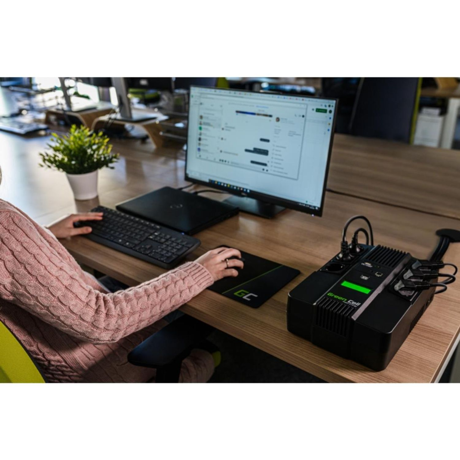 Kobieta pisząca na klawiaturze z monitorem, myszą i zasilaczem na biurku.