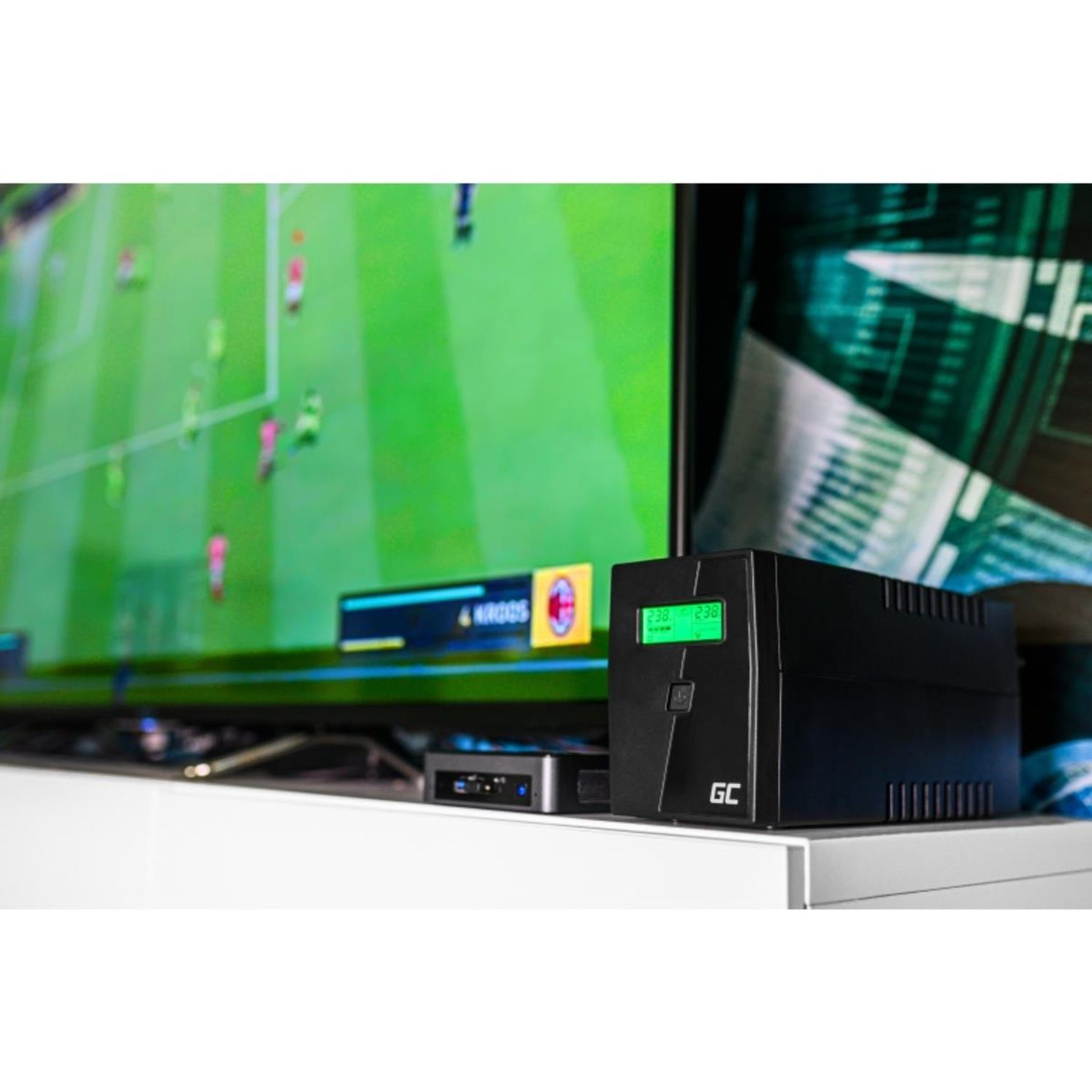 Czarne urządzenie UPS na białej półce, z telewizorem wyświetlającym mecz piłki nożnej.
