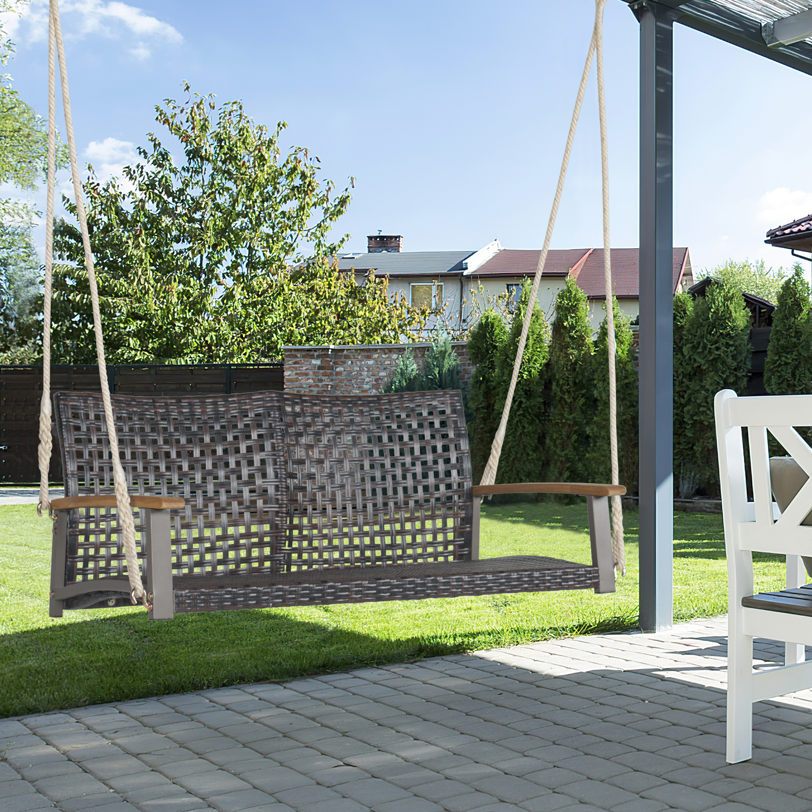 Korbschaukel auf einer Terrasse, umgeben von Grün und sonnigem Himmel.