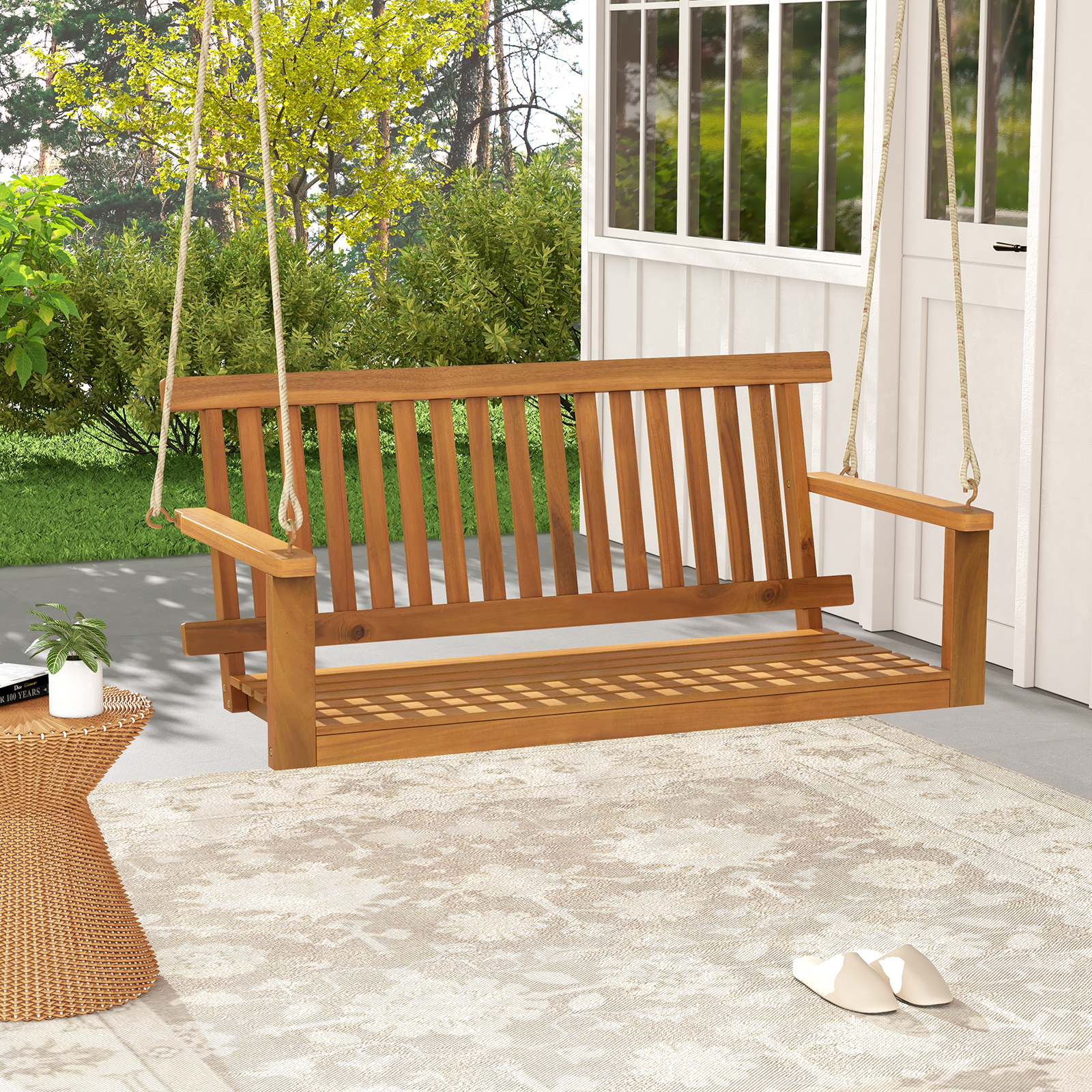 Hölzerne Schaukelbank an Seilen hängend, auf einer Veranda mit Teppich und Pflanzen.