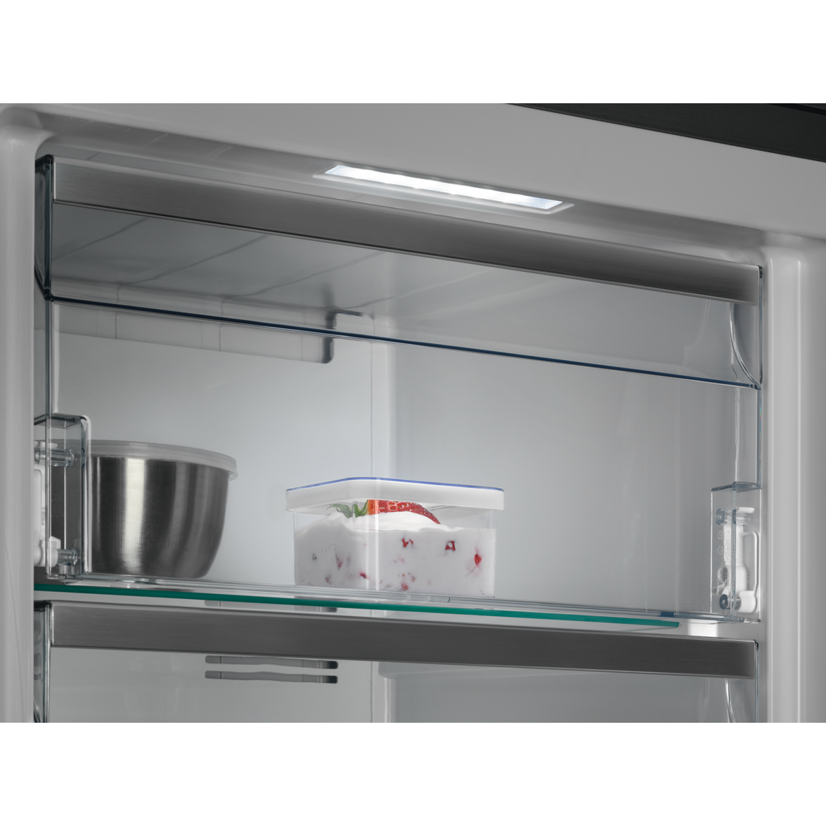 Dentro de un refrigerador con un estante transparente que contiene un recipiente con fresas.