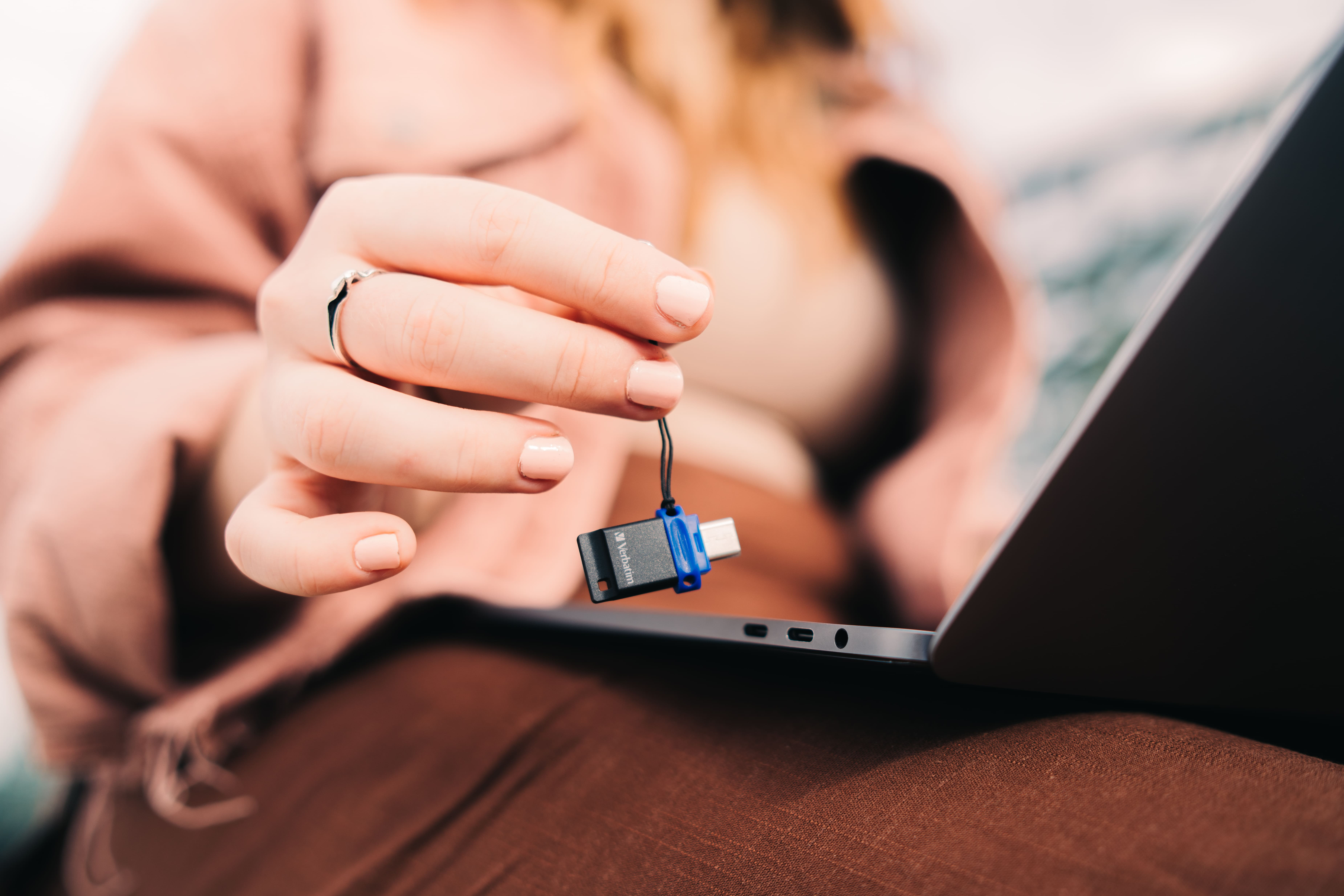 Osoba trzymająca niebieski pendrive. Laptop w tle.