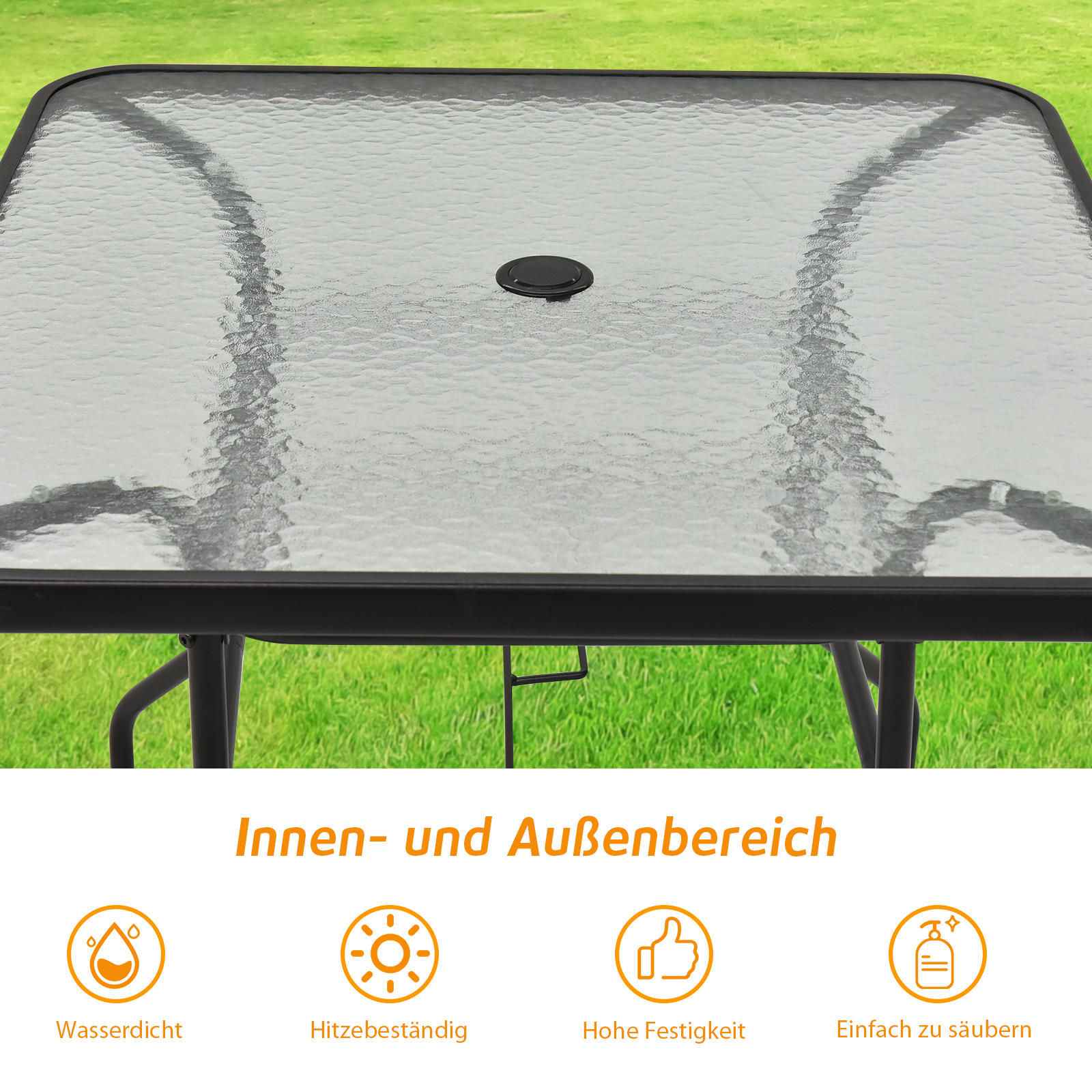 Ein Glastisch mit schwarzem Rahmen wird gezeigt, mit quadratischer Form. Der Hintergrund ist ein grüner Rasen.
