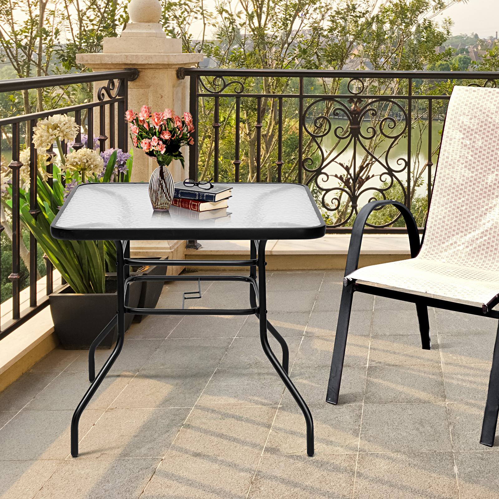 Ein Glastisch mit Blumen, Büchern und Brille, neben einem Stuhl auf einer Terrasse.