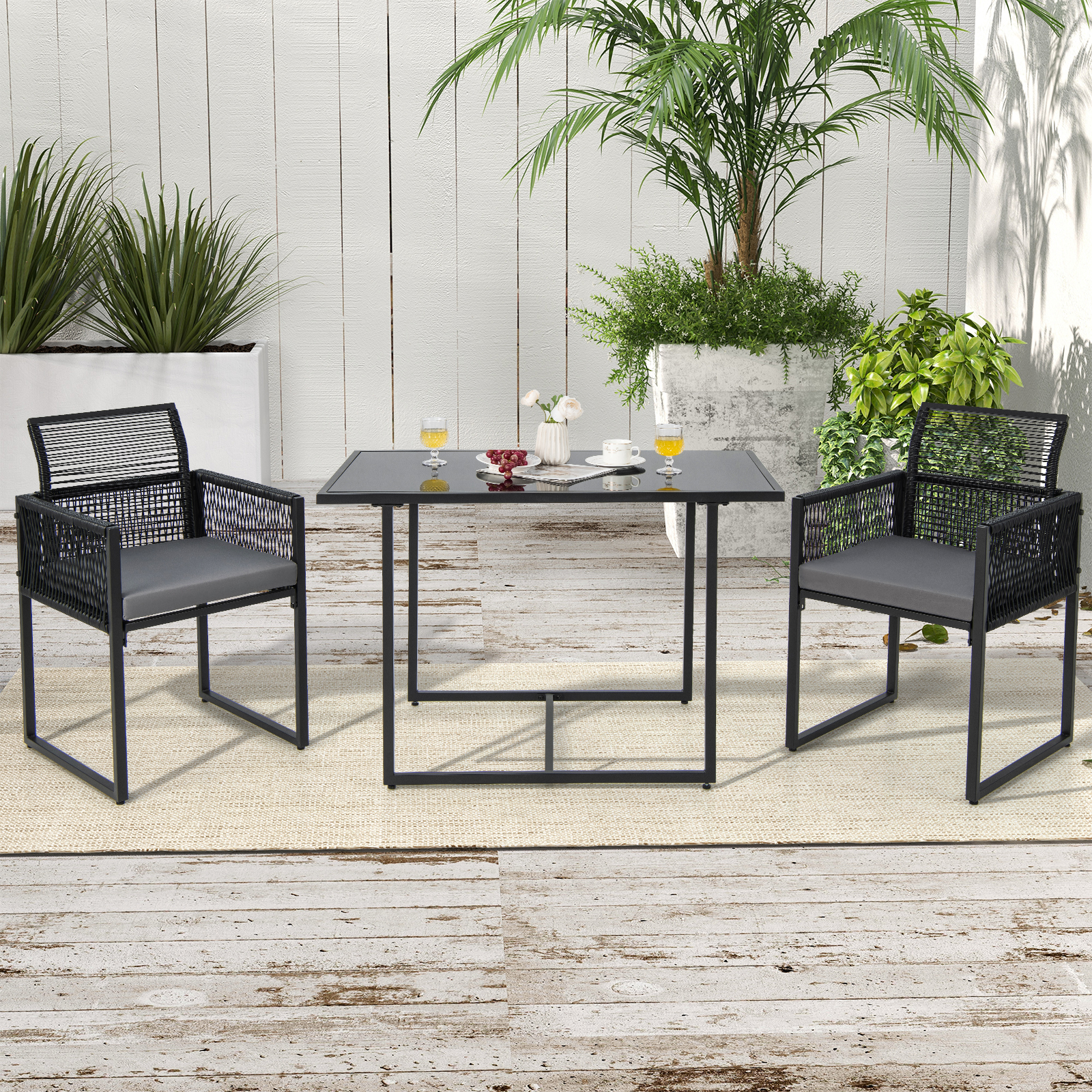 Terrassenmöbel im Freien. Schwarzer Tisch und Stühle mit grauen Kissen. Pflanzen und weißer Zaun im Hintergrund.