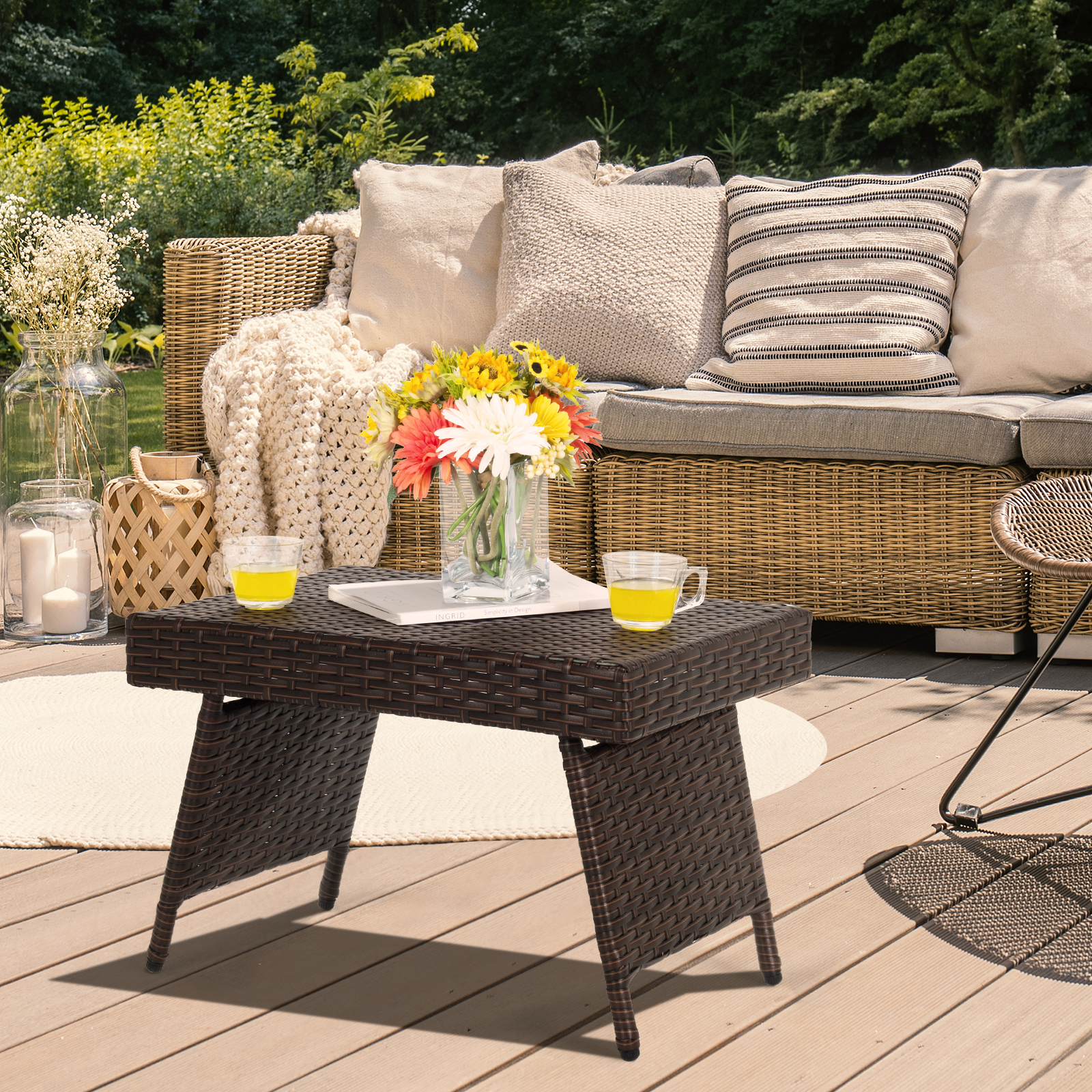 Rattantisch auf Holzterrasse mit Blumen und Getränken. Sofa im Hintergrund.